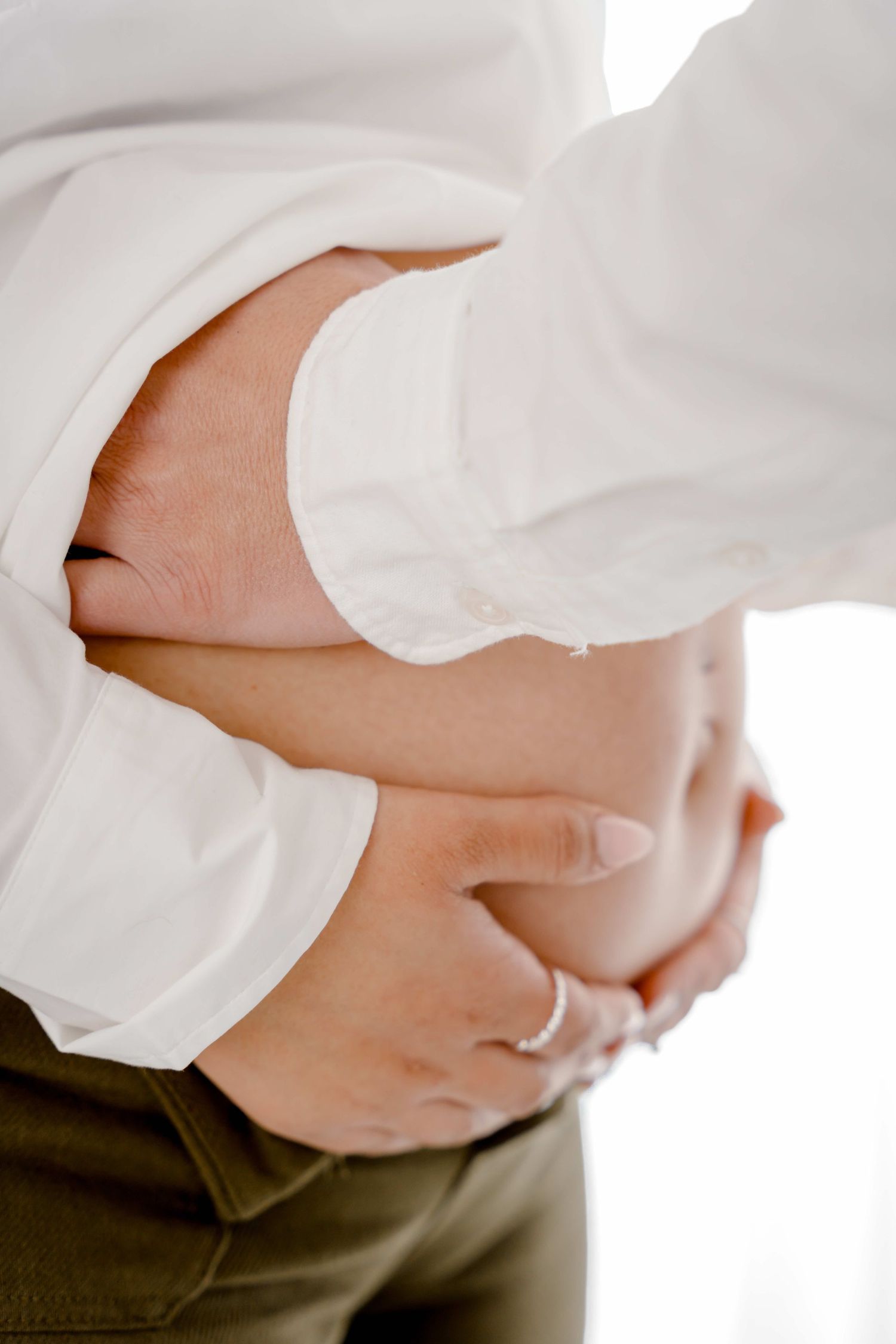 Close-up series of hands gently cradling a pregnant belly in white clothing against a dark background.