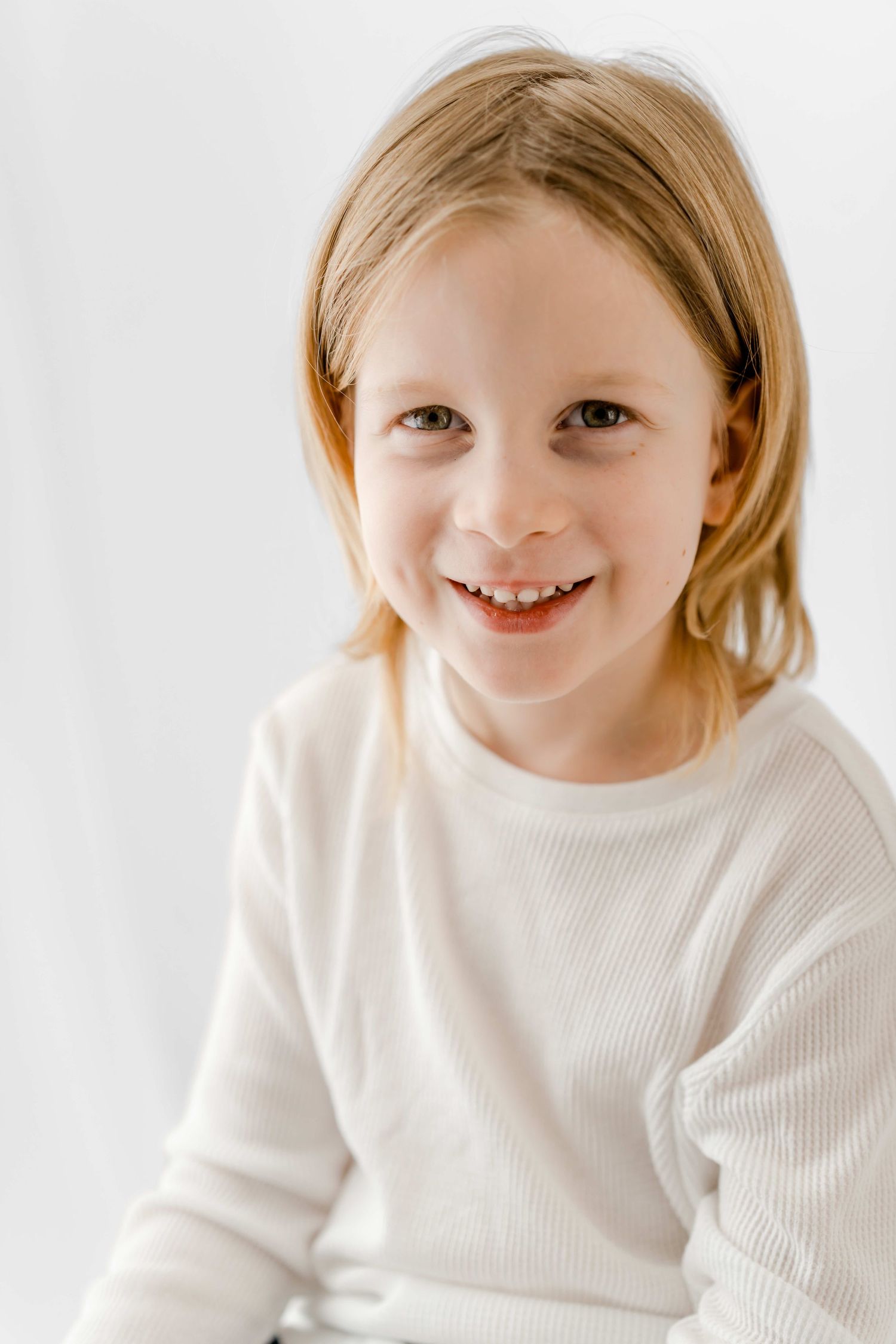 Child in white sweater shows joyful expressions in a series of candid portraits against light background.
