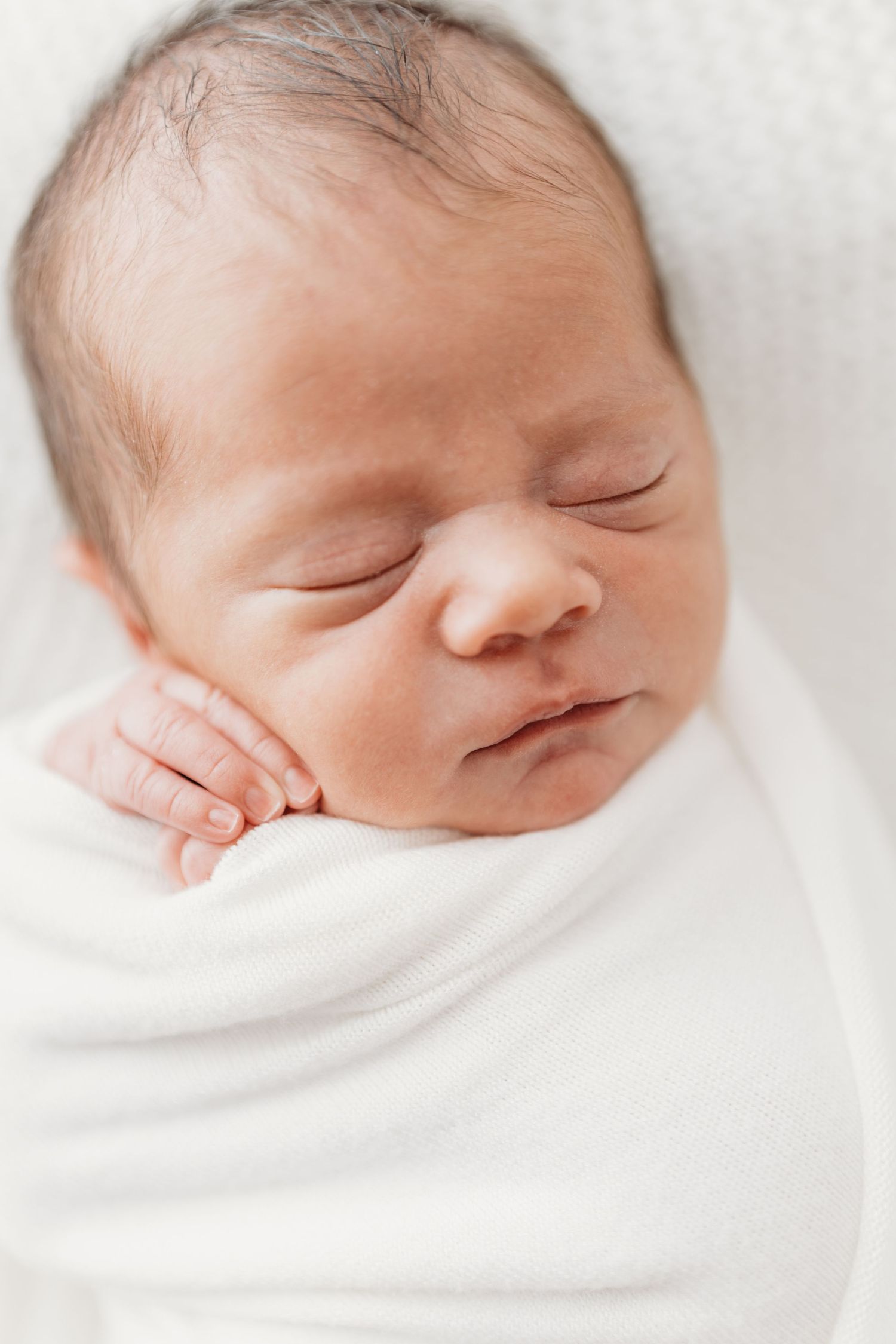 A series of four close-up photos showing a peaceful sleeping newborn baby wrapped in soft white blankets.