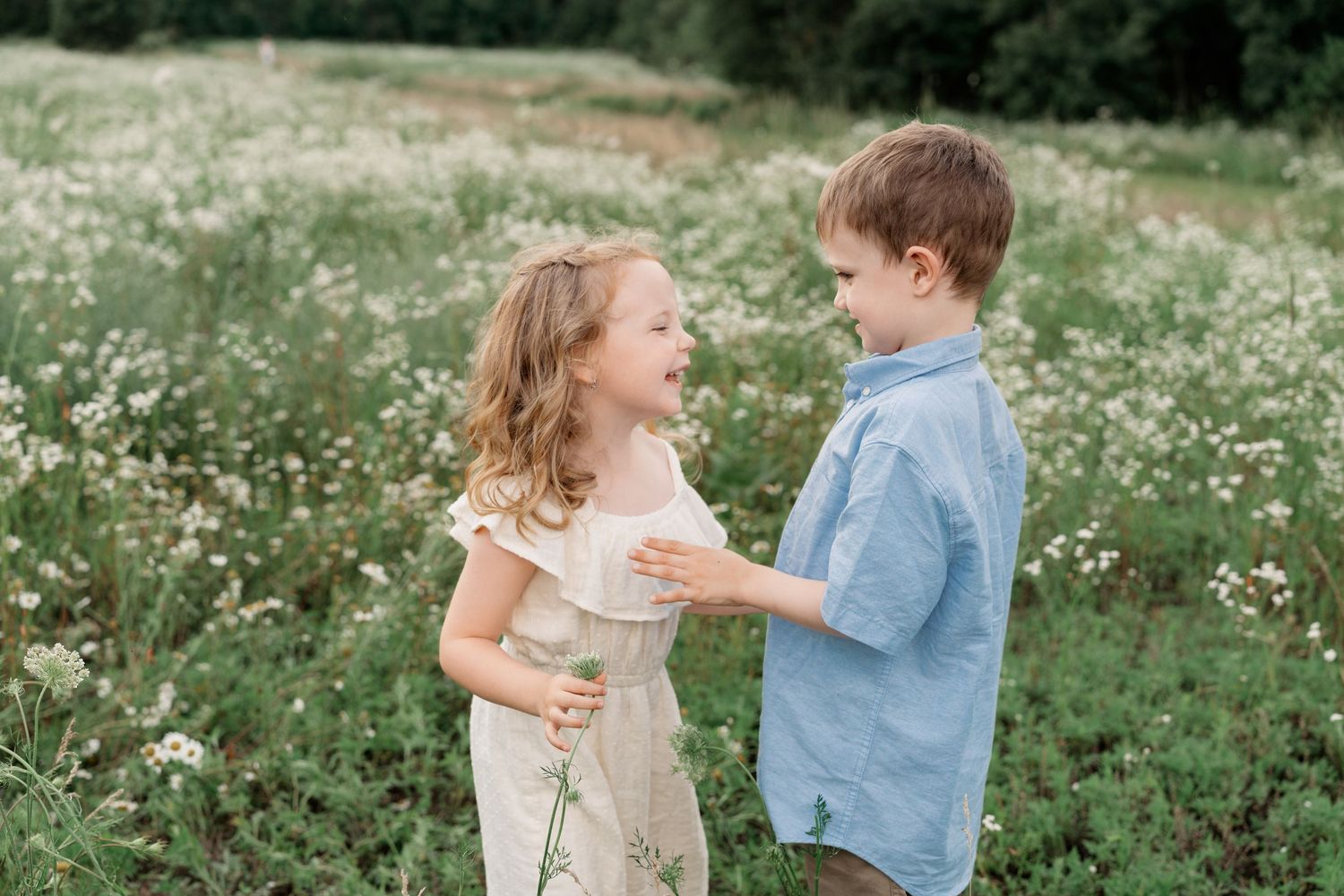 Two people share a tender moment in a blooming meadow filled with white wildflowers on a sunny summer day.