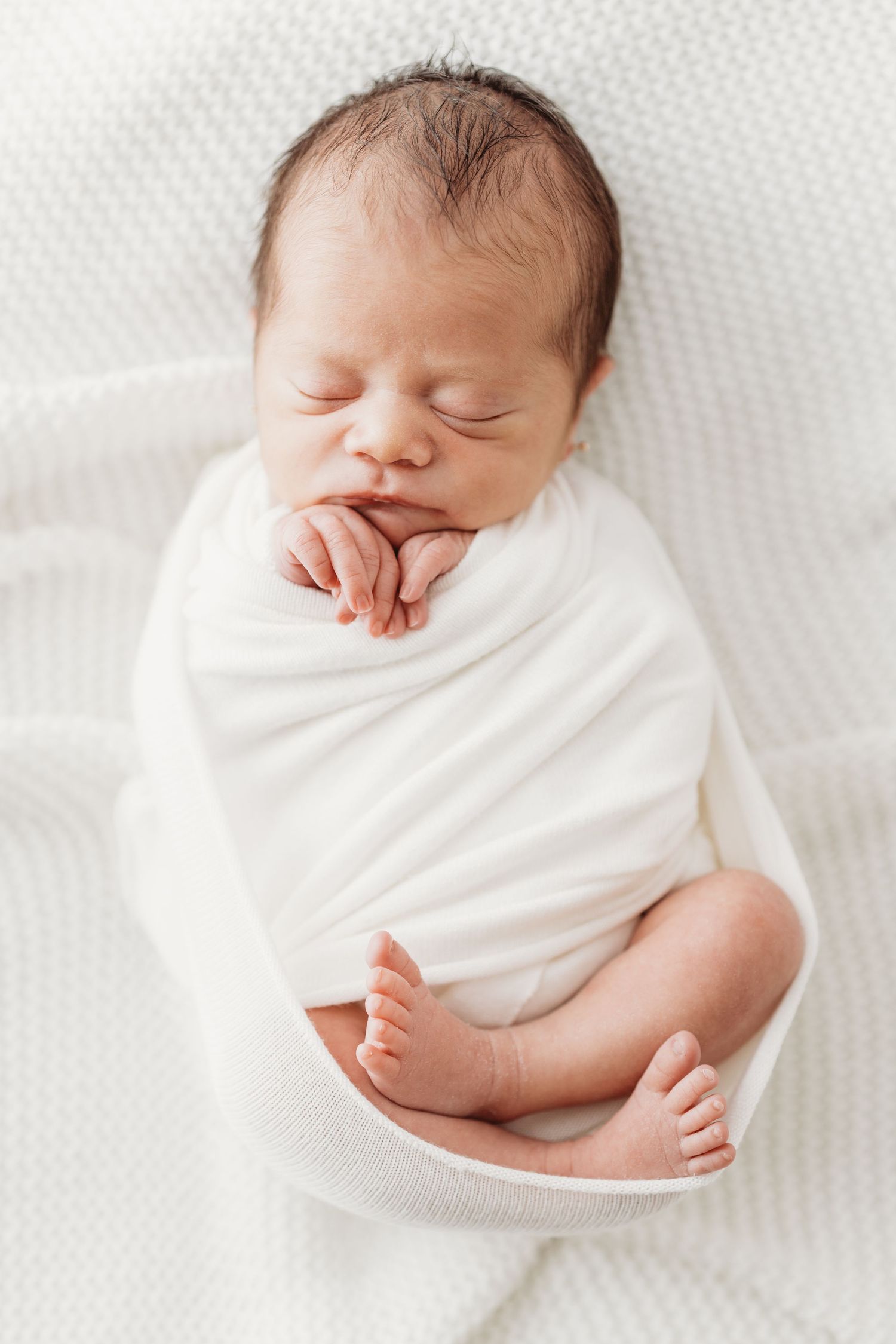Peaceful sleeping newborn baby wrapped in soft white swaddle blanket on white background.