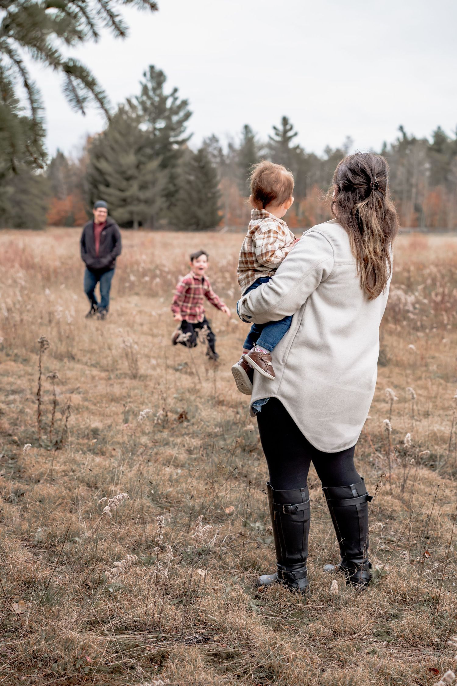 People walking together through a brown autumn field with evergreen trees in the background.