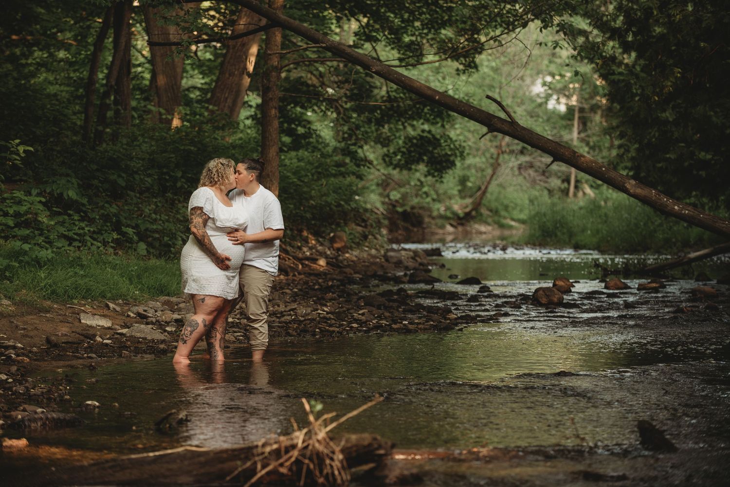 A couple shares a romantic moment together while standing in a scenic creek surrounded by lush forest.