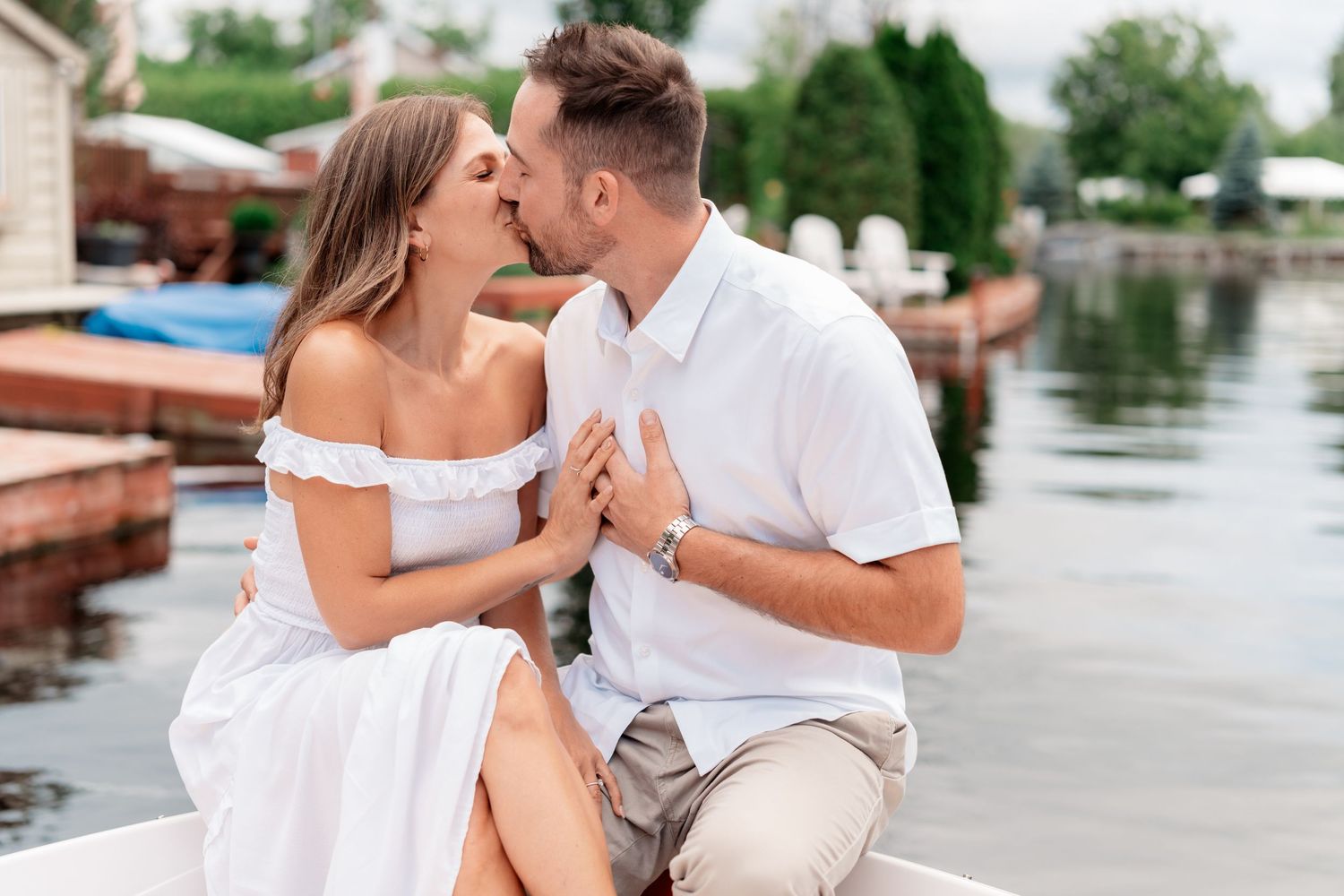 Romantic couple sharing tender moments on a dock by the water in matching white summer outfits.
