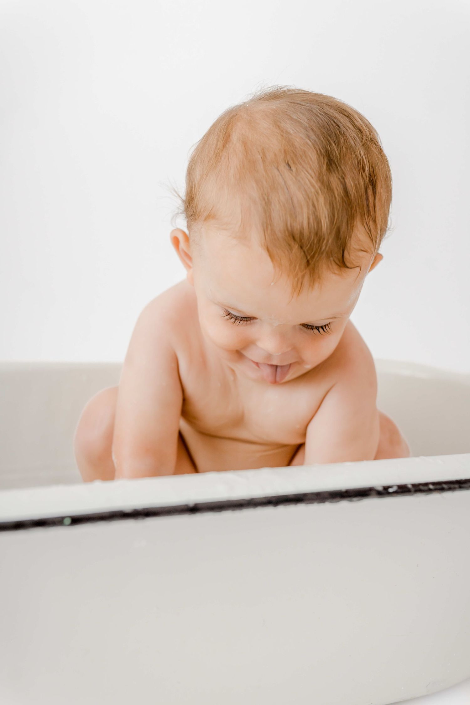 A baby peeks over the edge of a white surface in a minimalist studio setting.