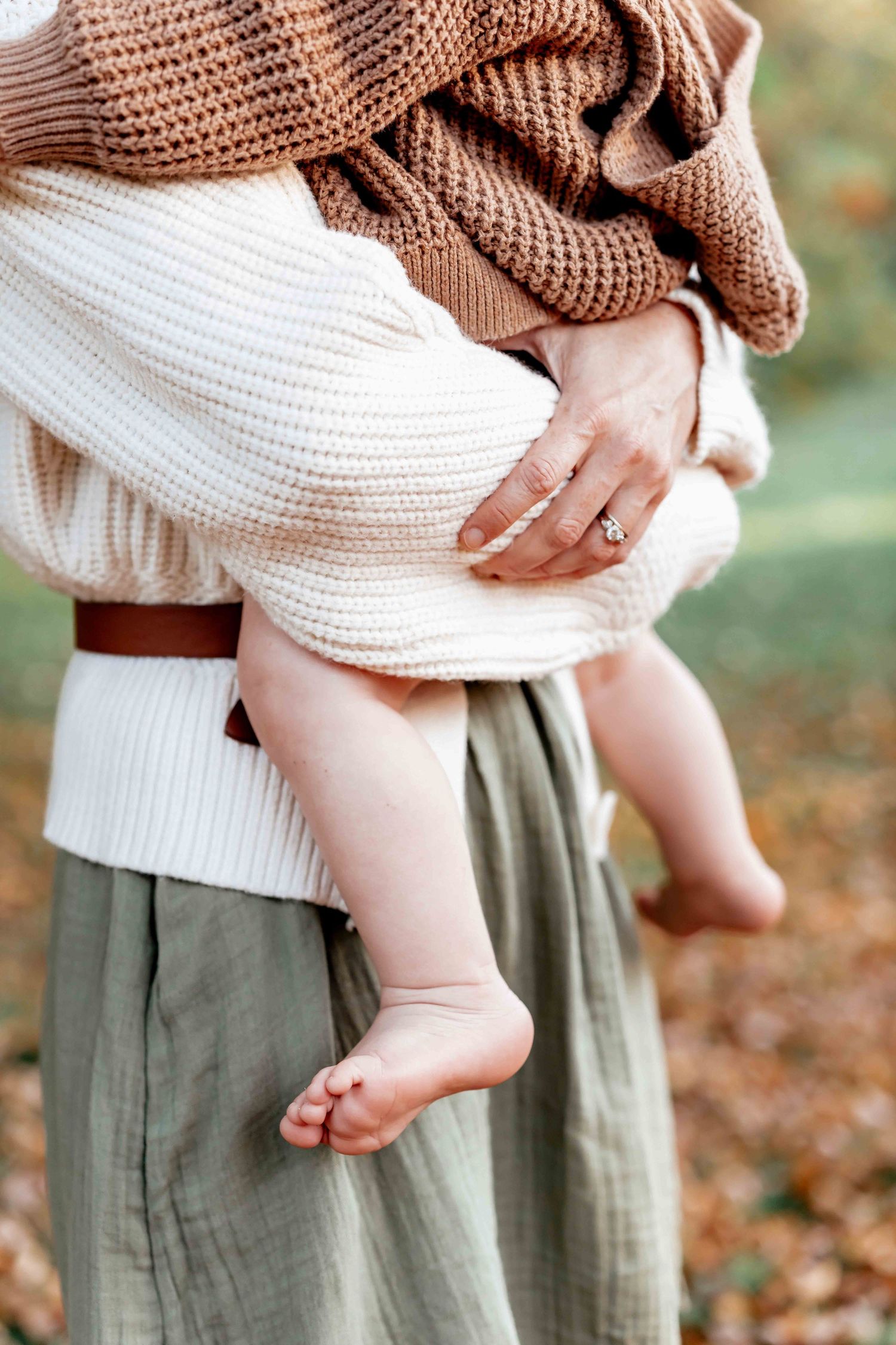 Close-up series of tiny bare baby feet being held against a cozy brown sweater and olive skirt in autumn.