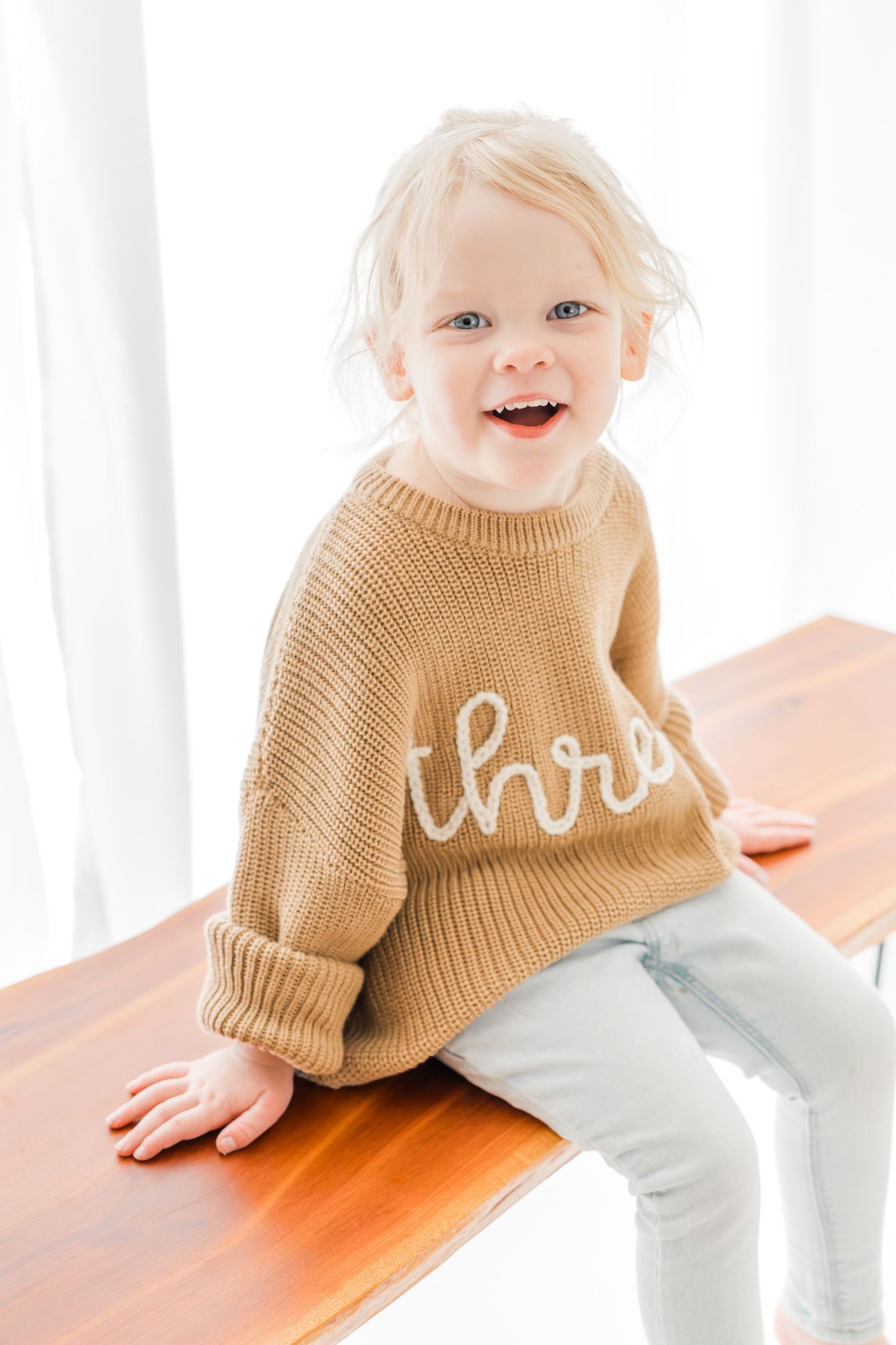 A series of three photos showing a small child in a brown knit sweater and light pants sitting on a wooden surface.