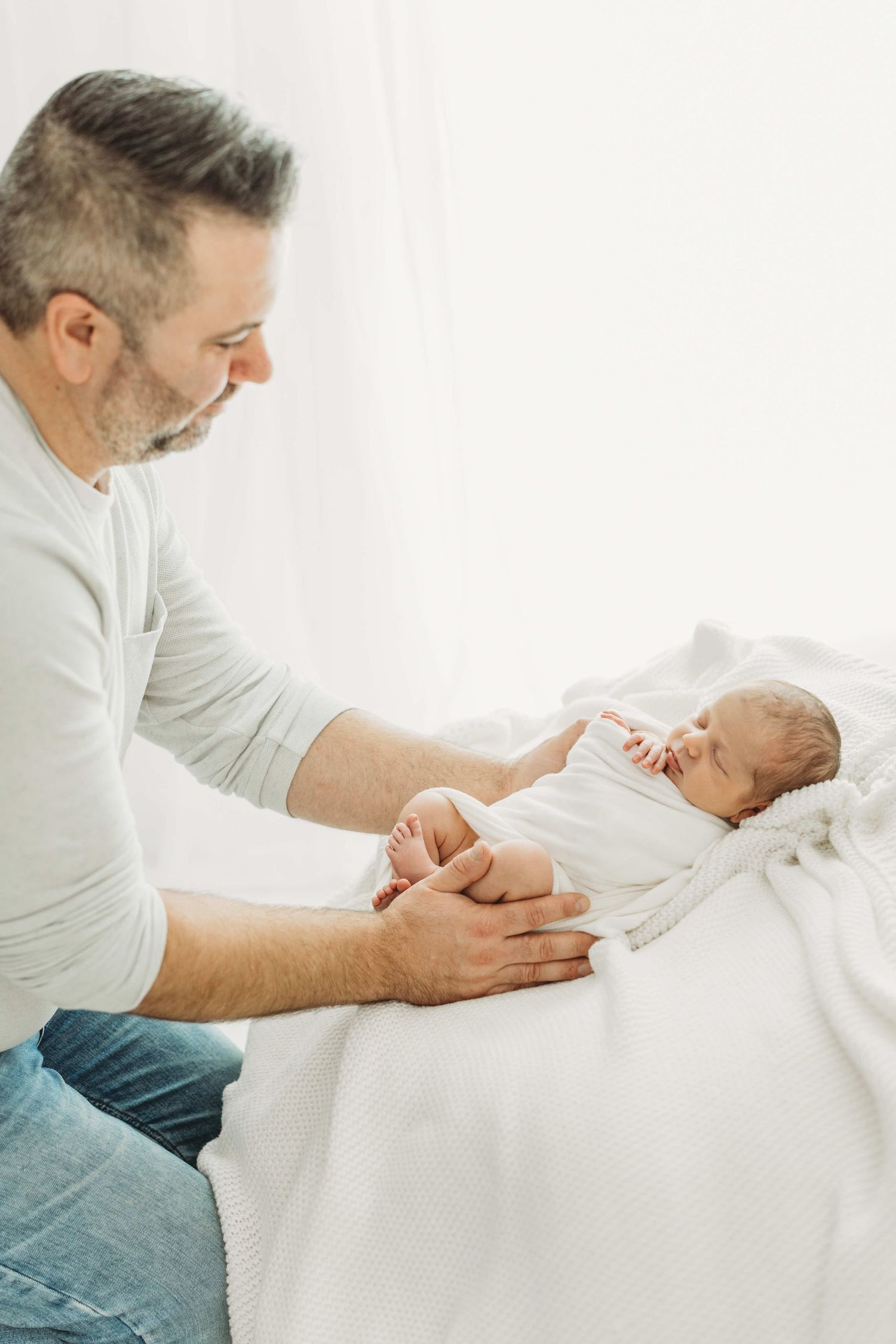 A tender moment between a parent and newborn baby while swaddled in soft white blankets.
