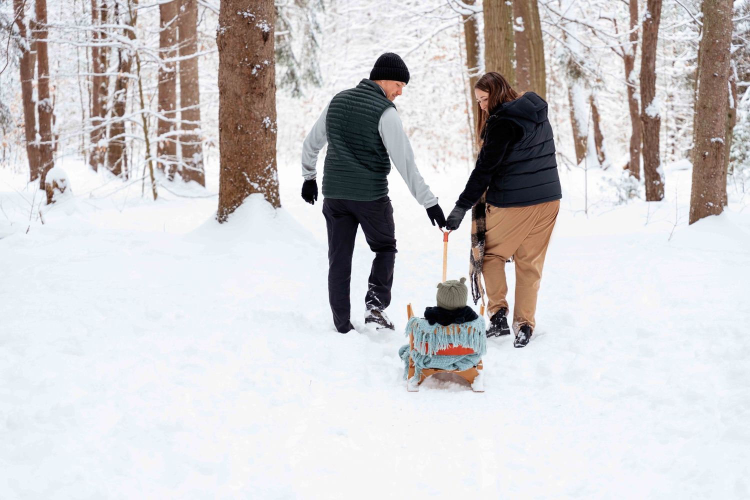 Winter family scene with people pulling sleds through snowy forest path.