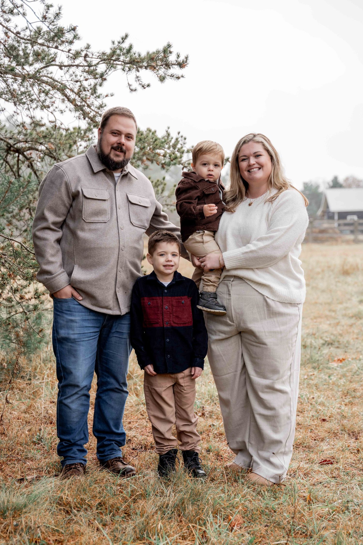 A family in coordinated neutral outfits poses together outdoors in a natural field setting during autumn.
