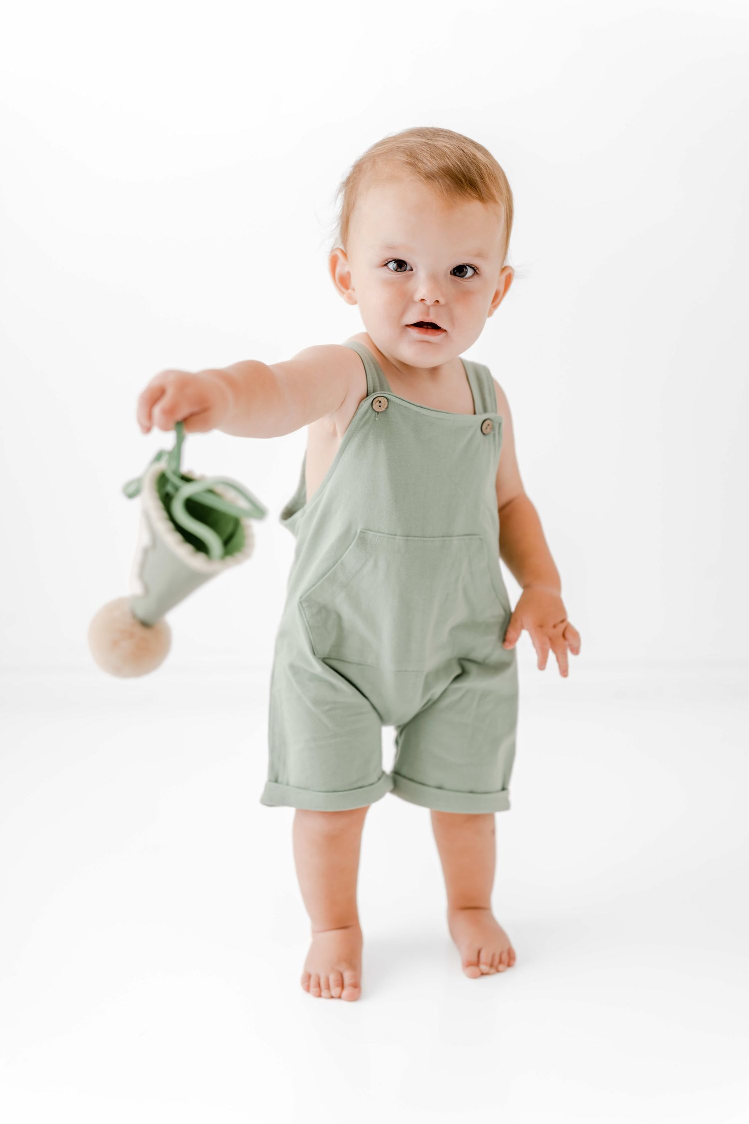Baby wearing sage green romper shown in three poses against white background, holding small object in last photo.