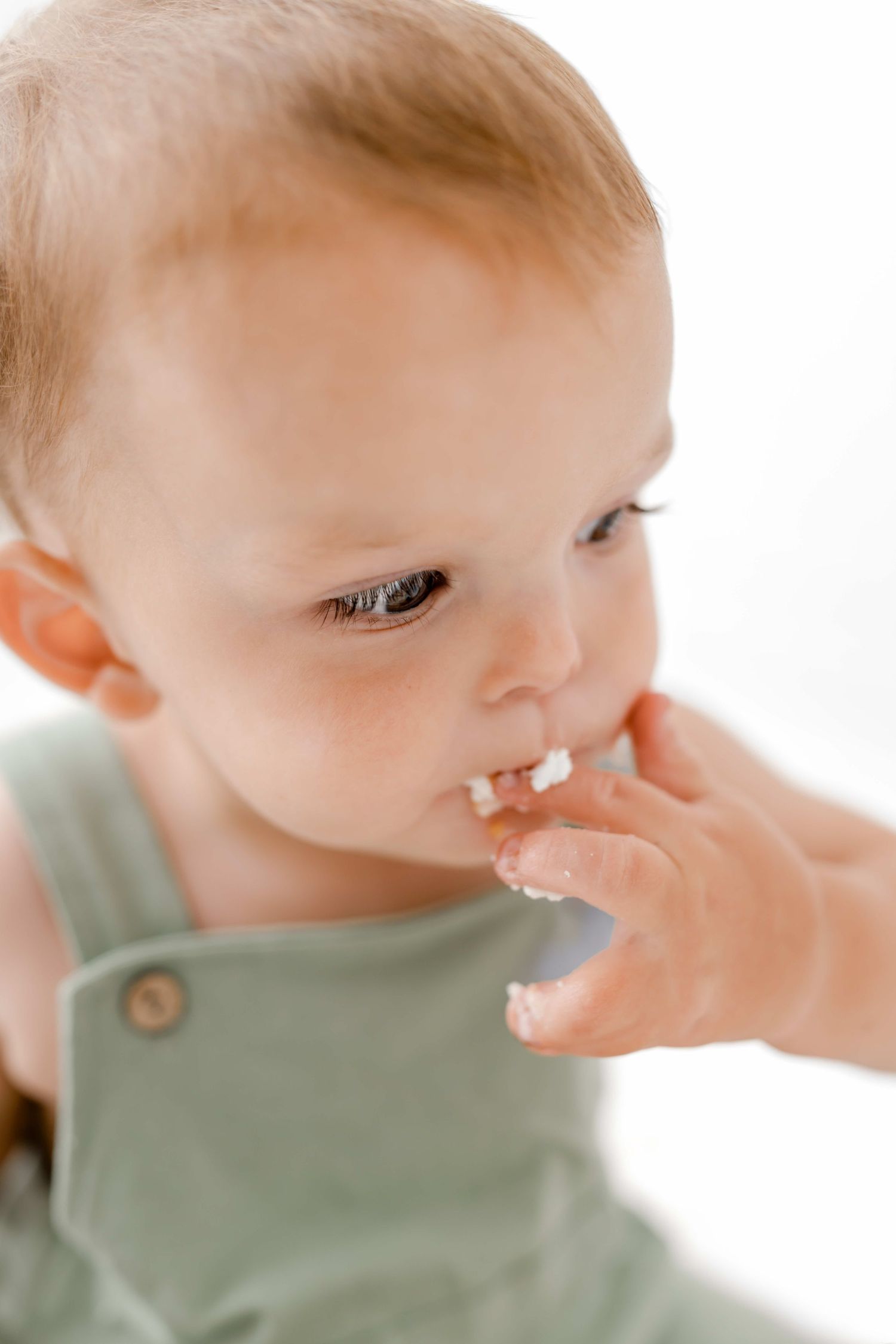 Baby in sage green shirt wipes nose with tissue in series of close-up shots.