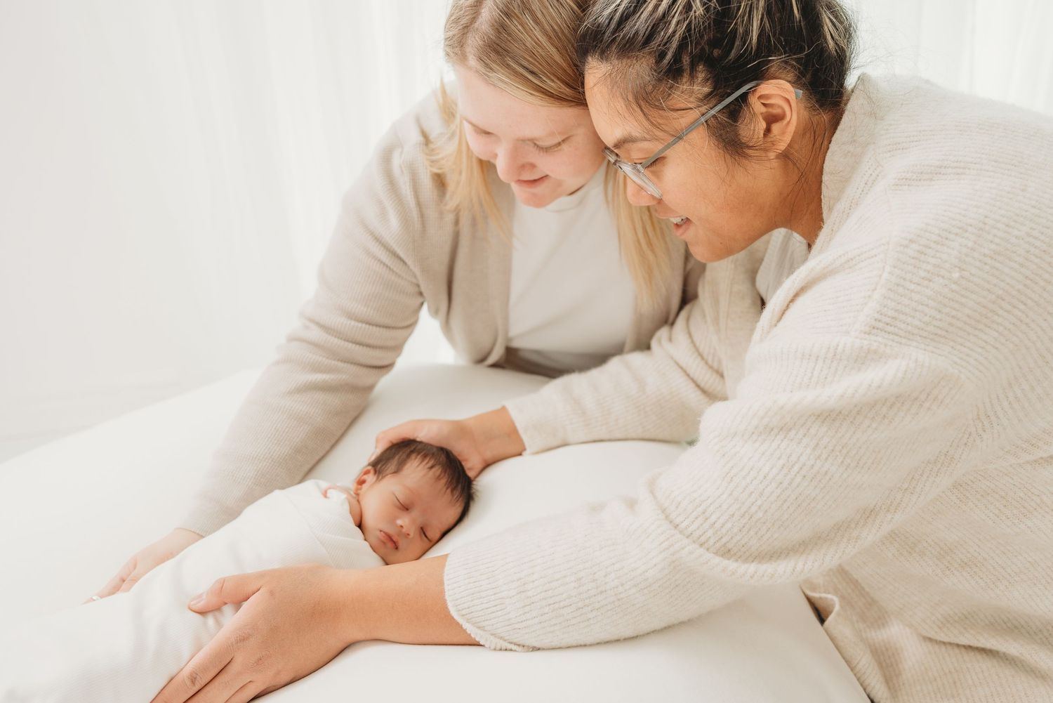Parent and baby lying together on white bedding while sharing tender bonding moments.