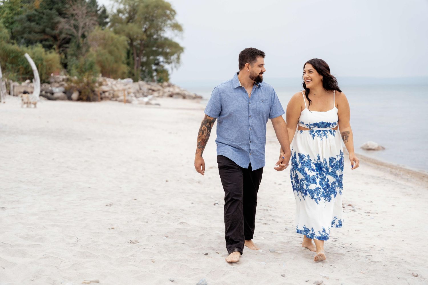 Couple walking hand in hand along a pristine white sandy beach wearing blue and white coordinated outfits.