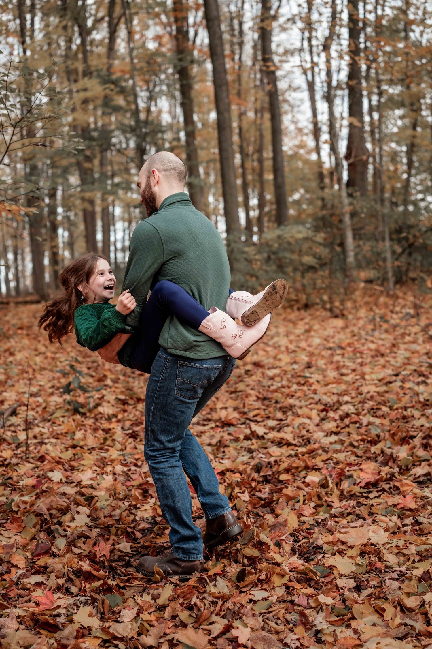 A playful autumn scene shows two people having fun in fallen leaves on a forest floor during fall.