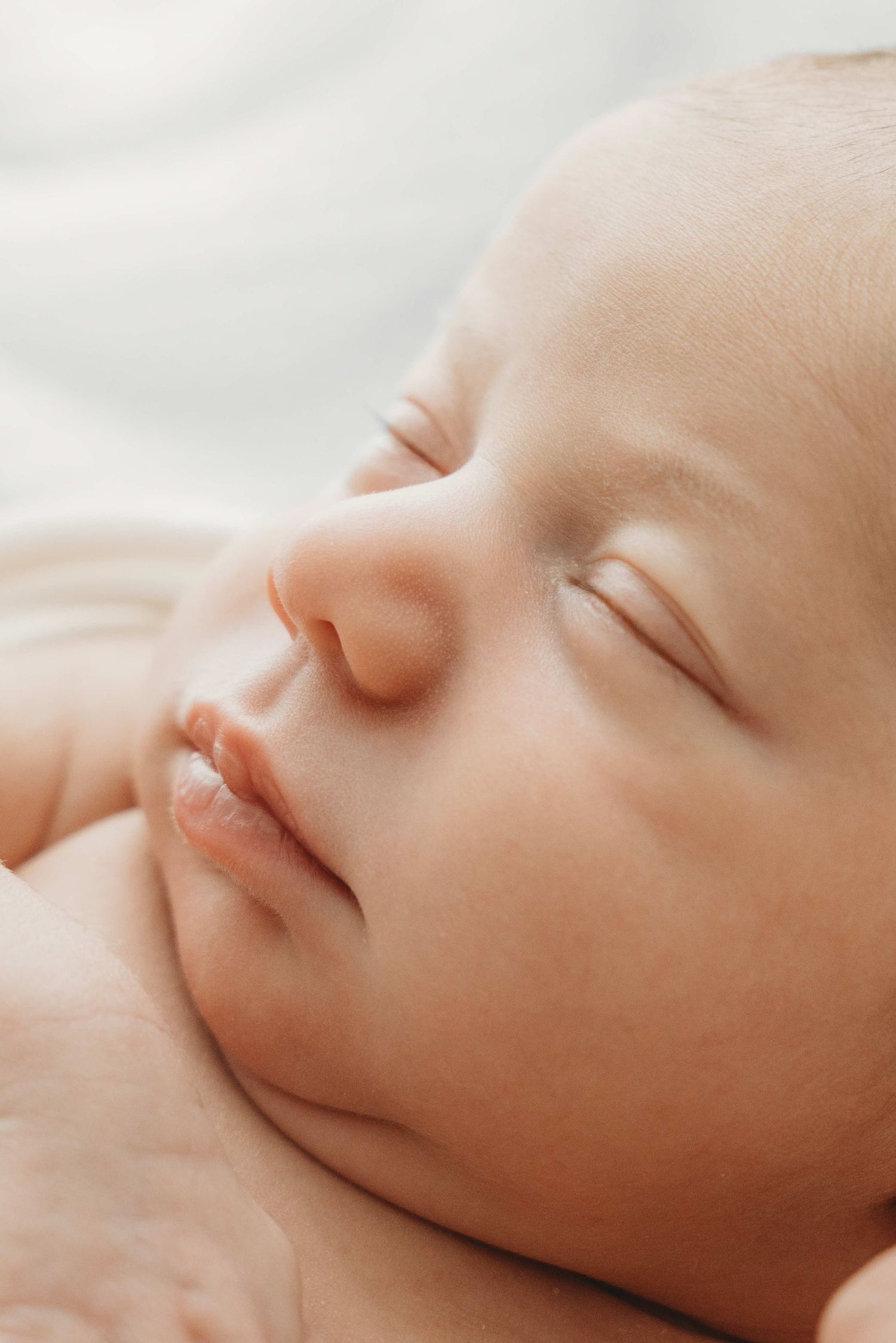 A sleeping baby's face in close-up view shows peaceful expression with soft lighting and gentle features.