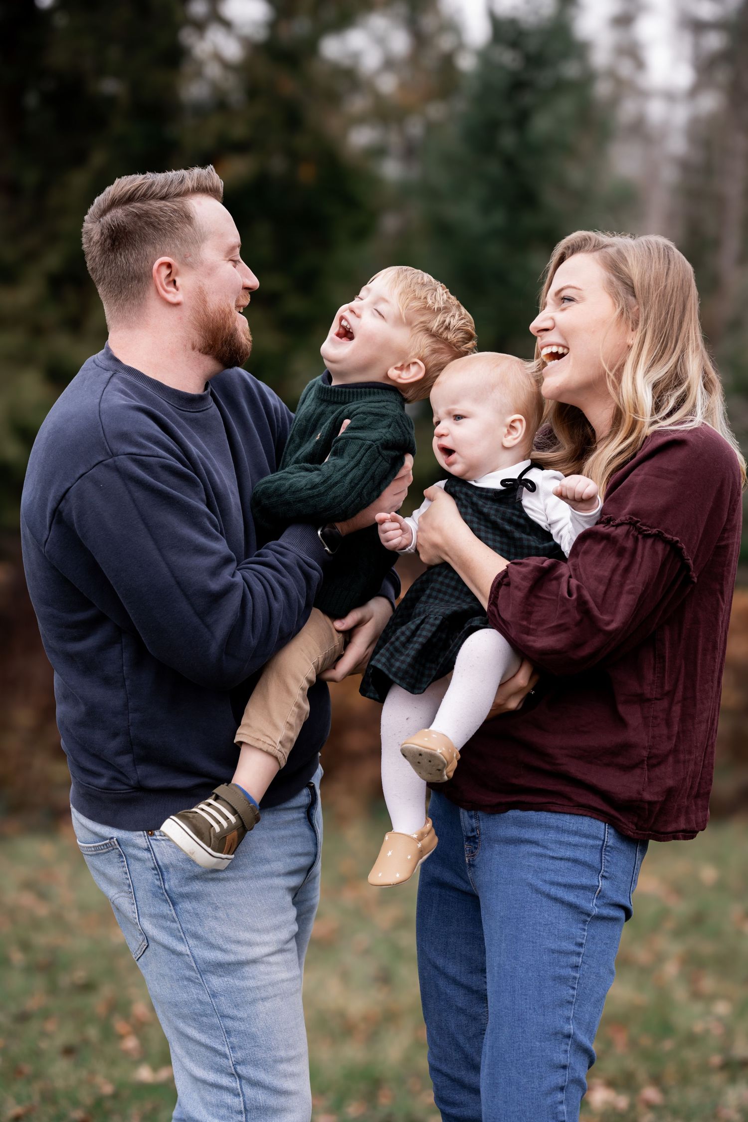 A family shares joyful laughter together outdoors during an autumn photoshoot in a park setting.