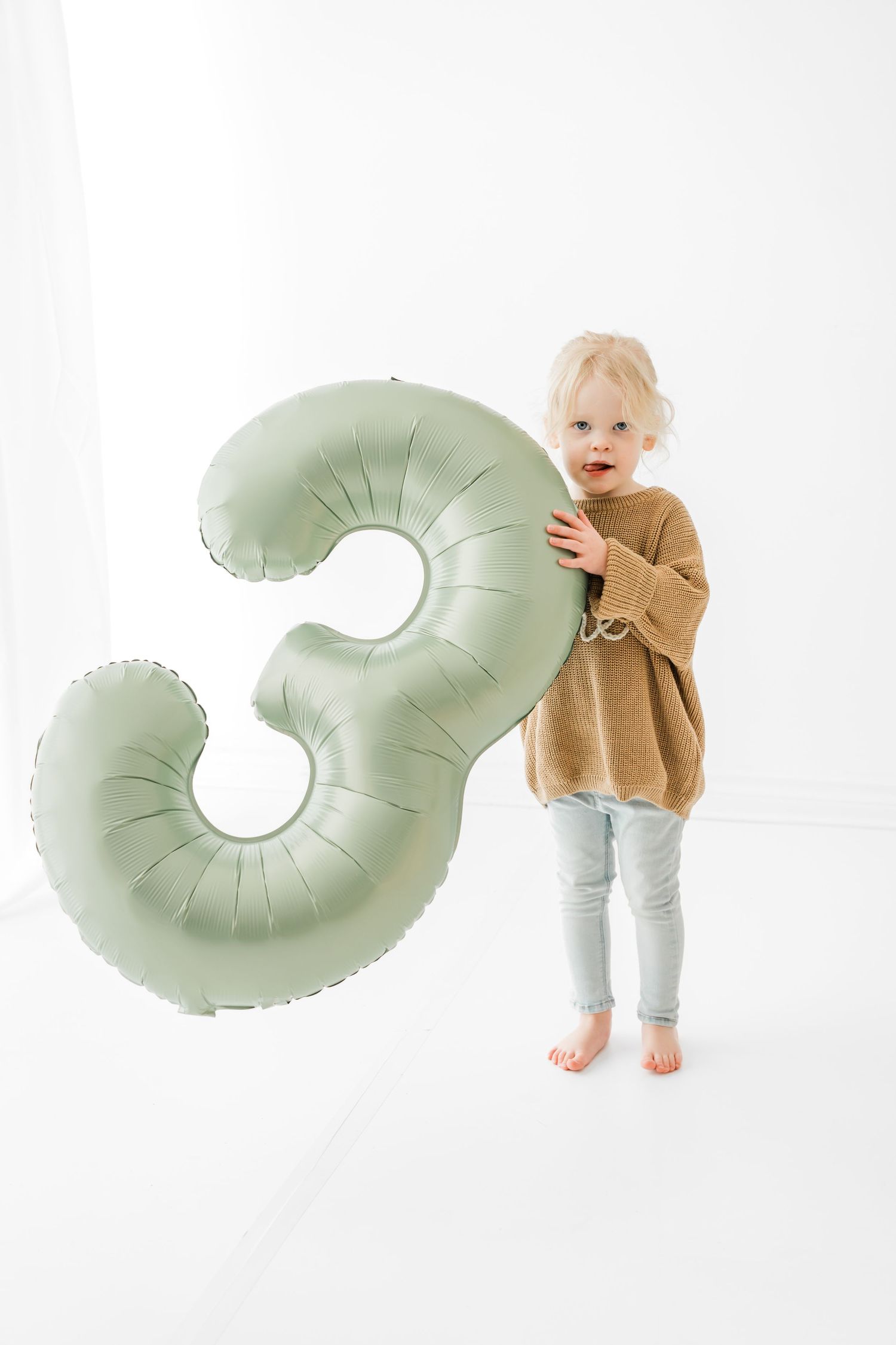 A series of images showing a toddler in brown sweater interacting with a mint green donut-shaped pillow against white background.