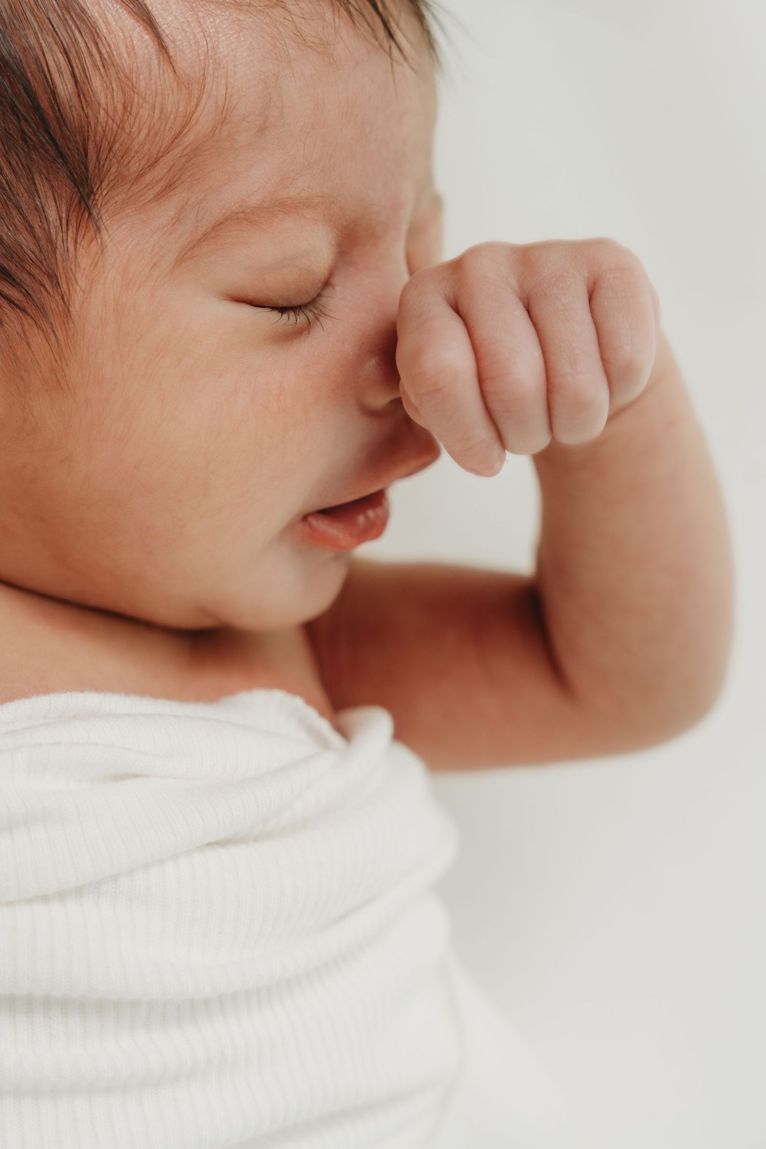 A tender moment captured in soft lighting as a baby rests peacefully in white fabric.