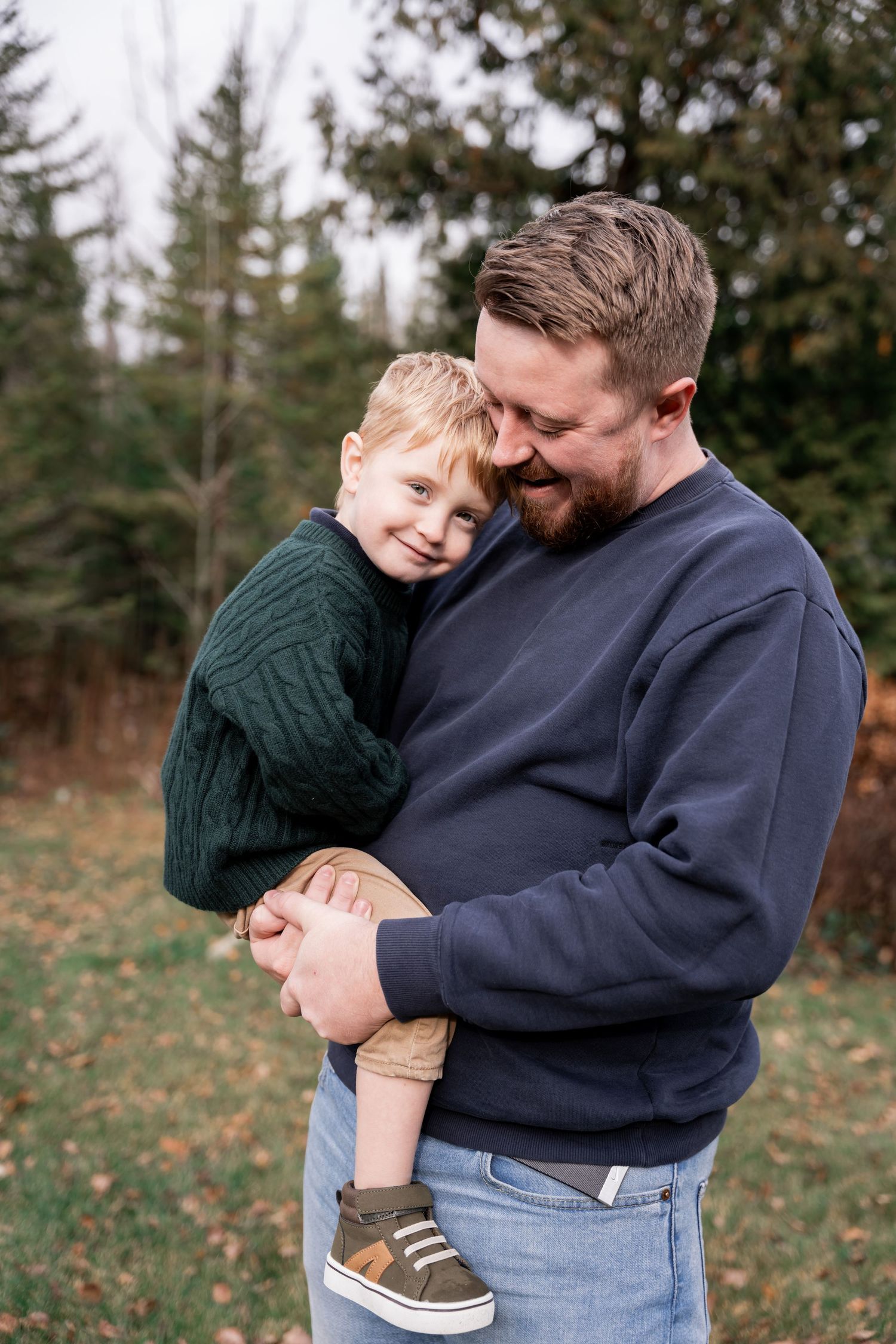 A tender moment shared between parent and child embracing outdoors against an evergreen forest backdrop.