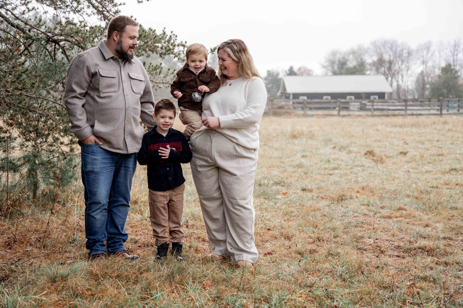 A family stands together in a misty field on an autumn morning wearing cozy sweaters and casual attire.