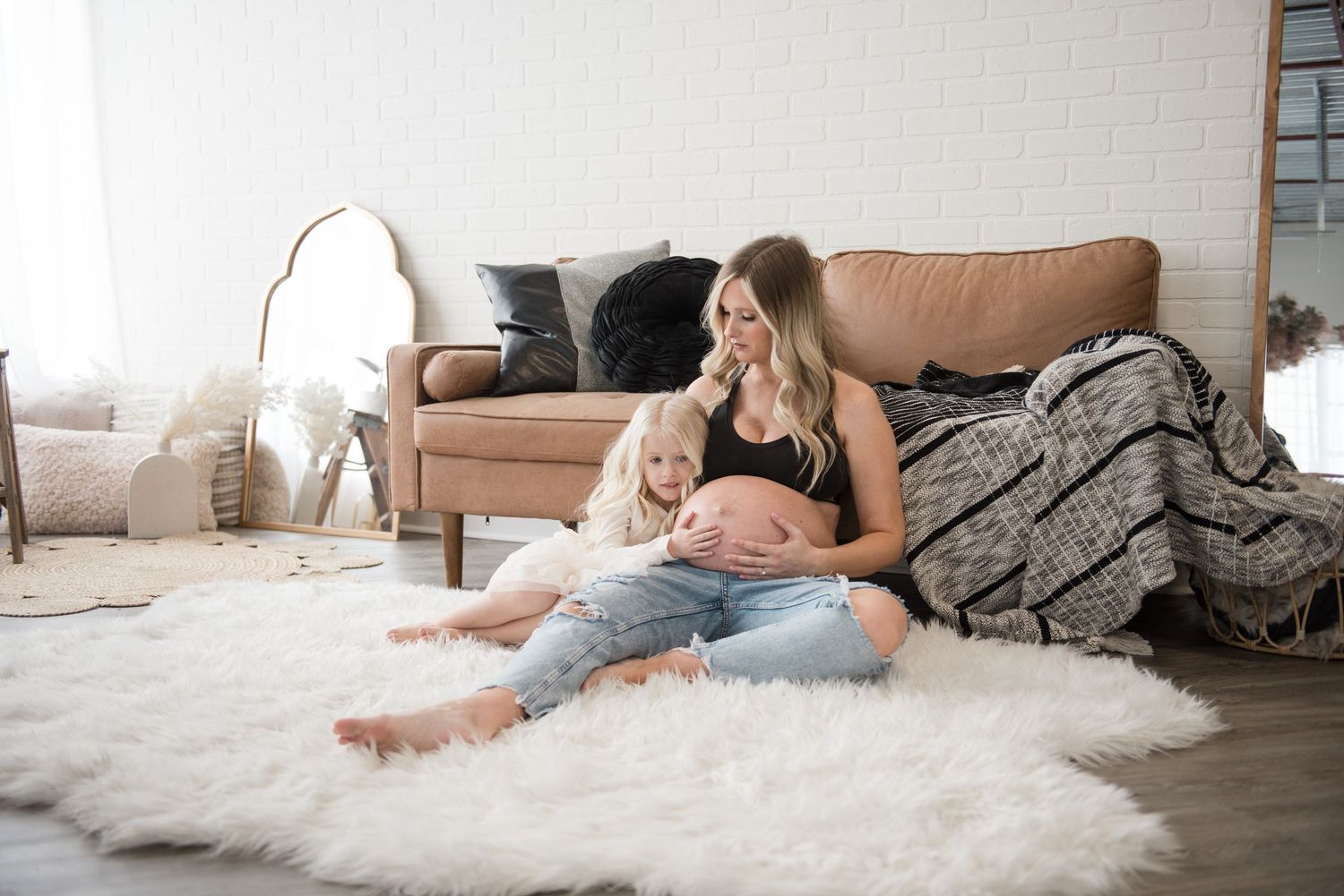 A pregnant woman relaxes on a plush white rug sharing a quite moment with her young daughter who is snuggled up next to her