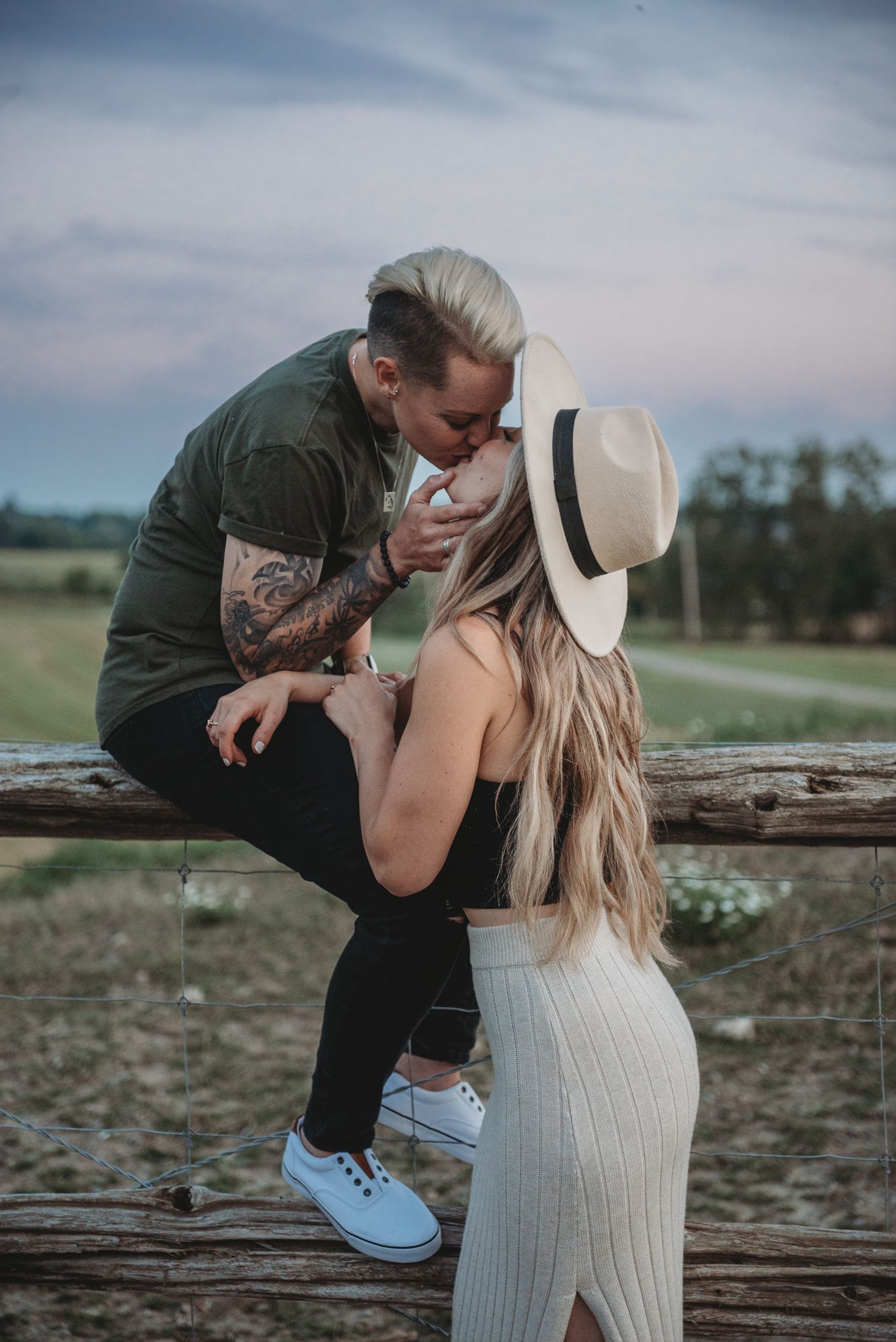 A romantic couple shares tender moments while sitting on rustic wooden logs in a scenic countryside setting.