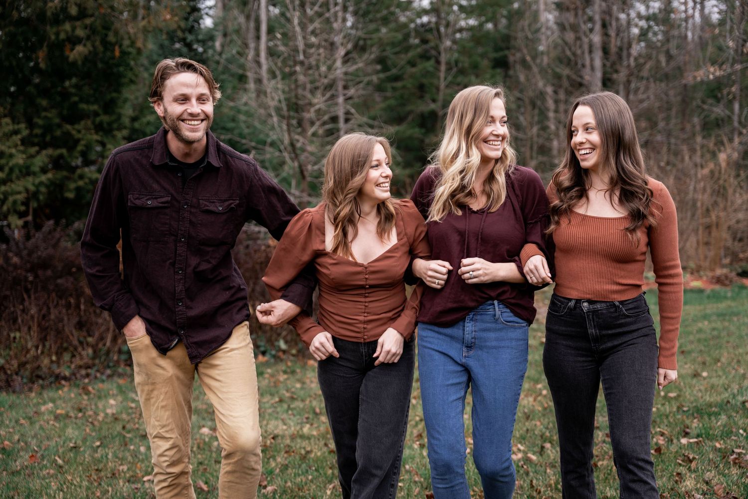 Siblings laughing together and walking across a grassy field during fall.