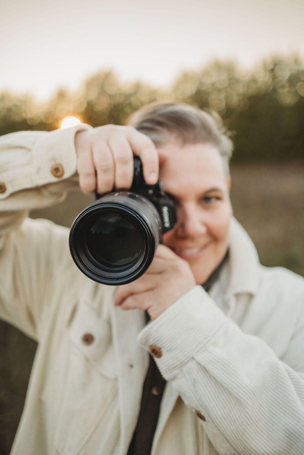 A photographer in a white sweater holds up a camera lens in a series of similar shots at sunset.