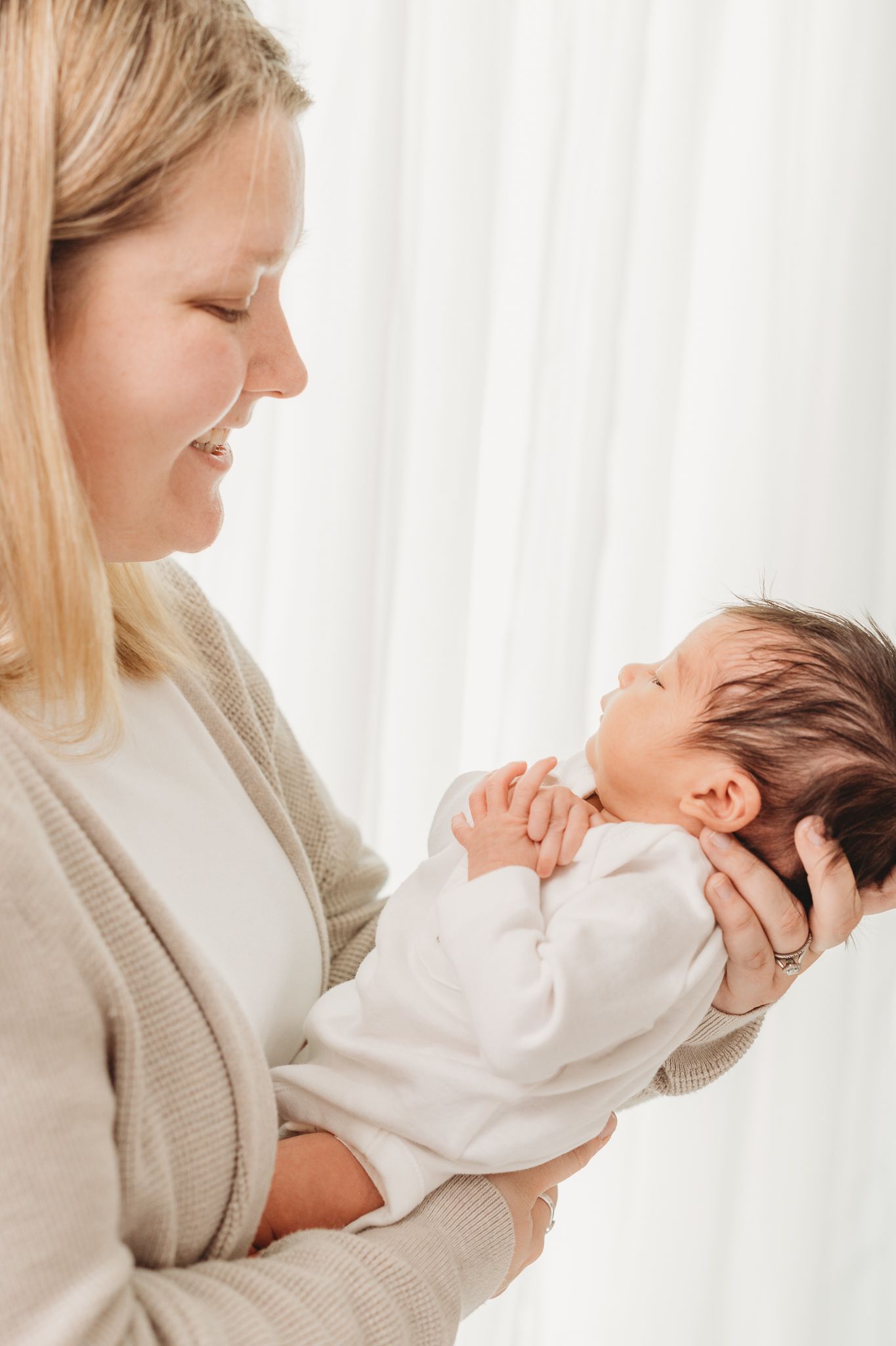 A tender moment captured in white as a parent cradles a sleeping newborn baby against a bright background.