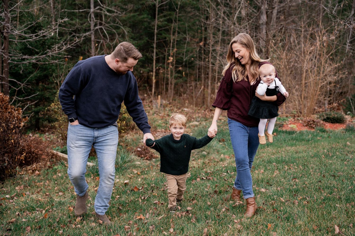 A family walks together through a wooded area during an outdoor photo session in autumn.