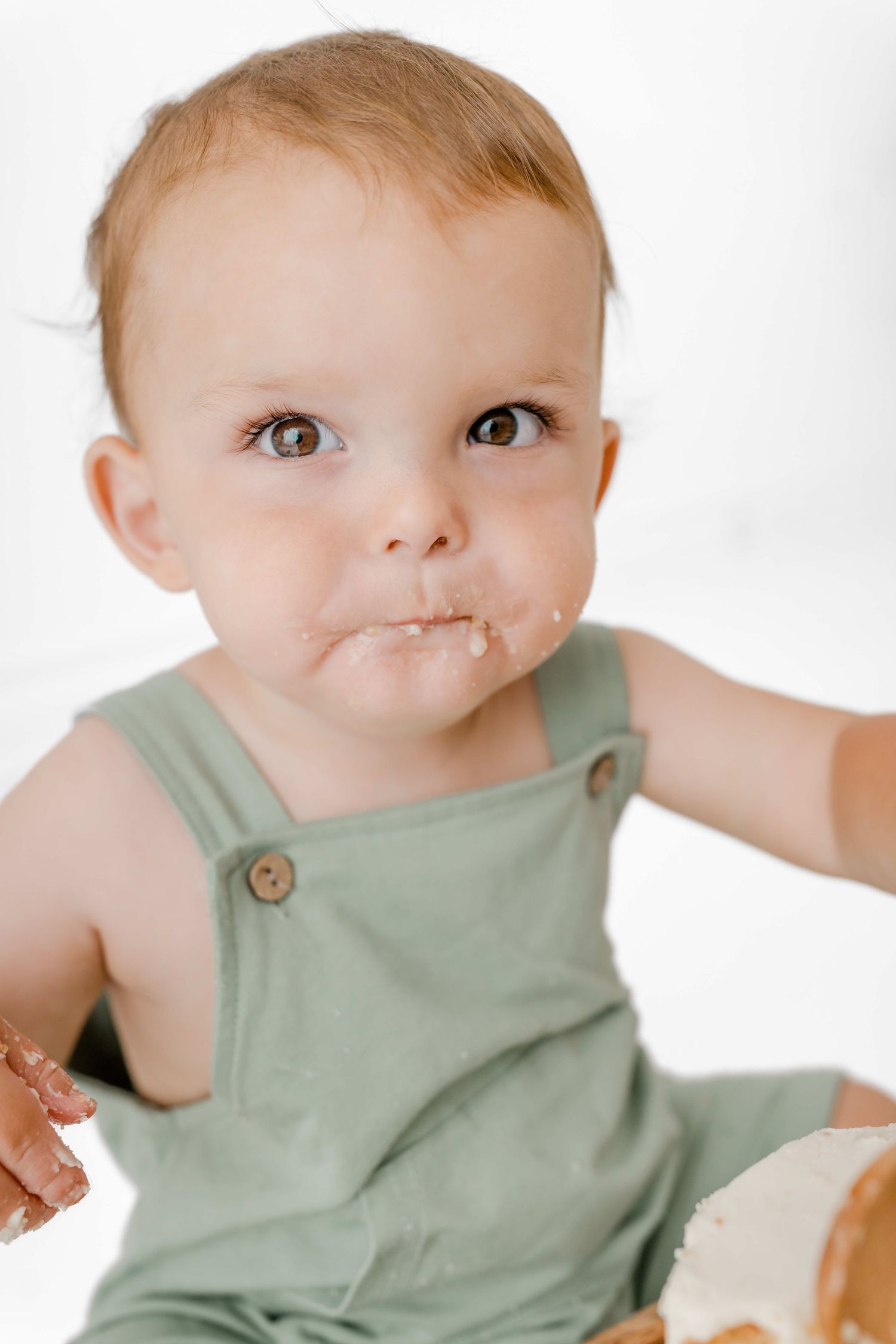 Close up view of a baby wearing a sage green sleeveless romper against a white background.
