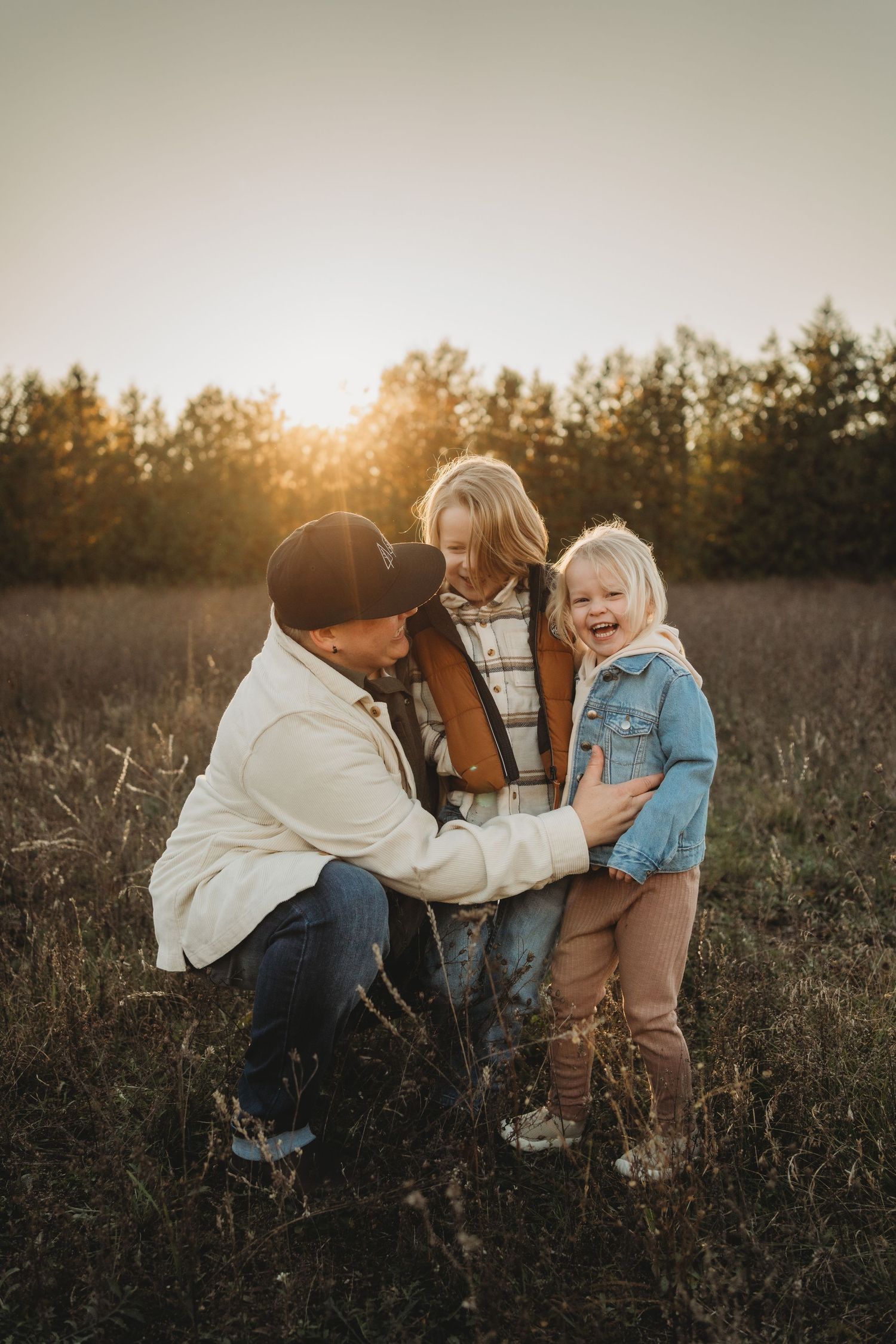 A heartwarming outdoor family moment captured at sunset in a golden field with trees in the background.