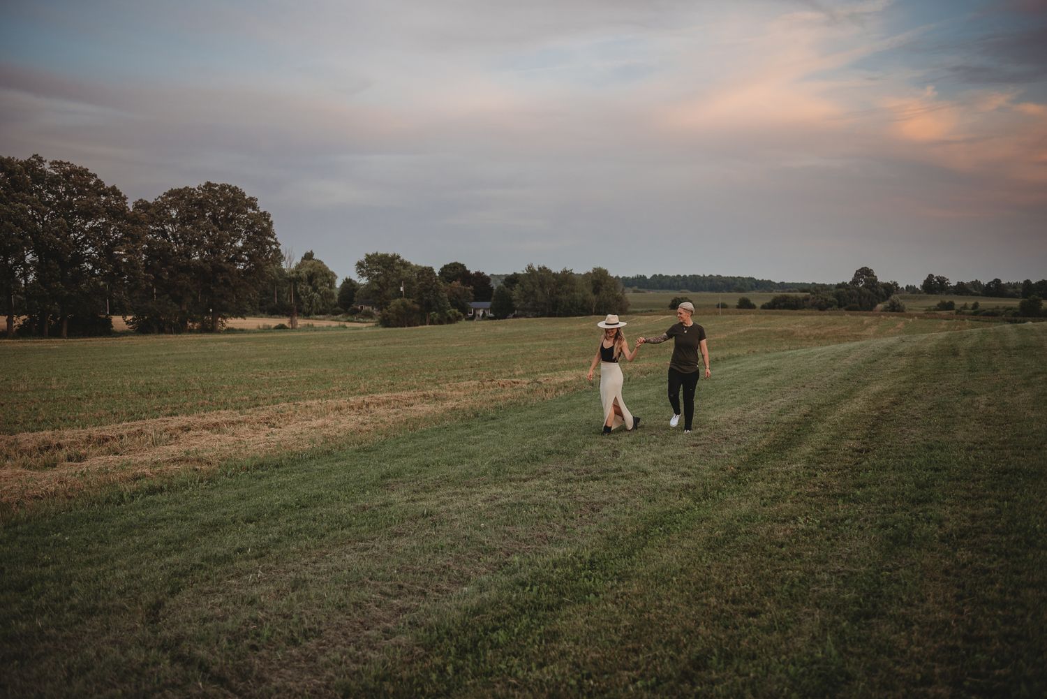 Two people strolling along a rural path through open fields during sunset.