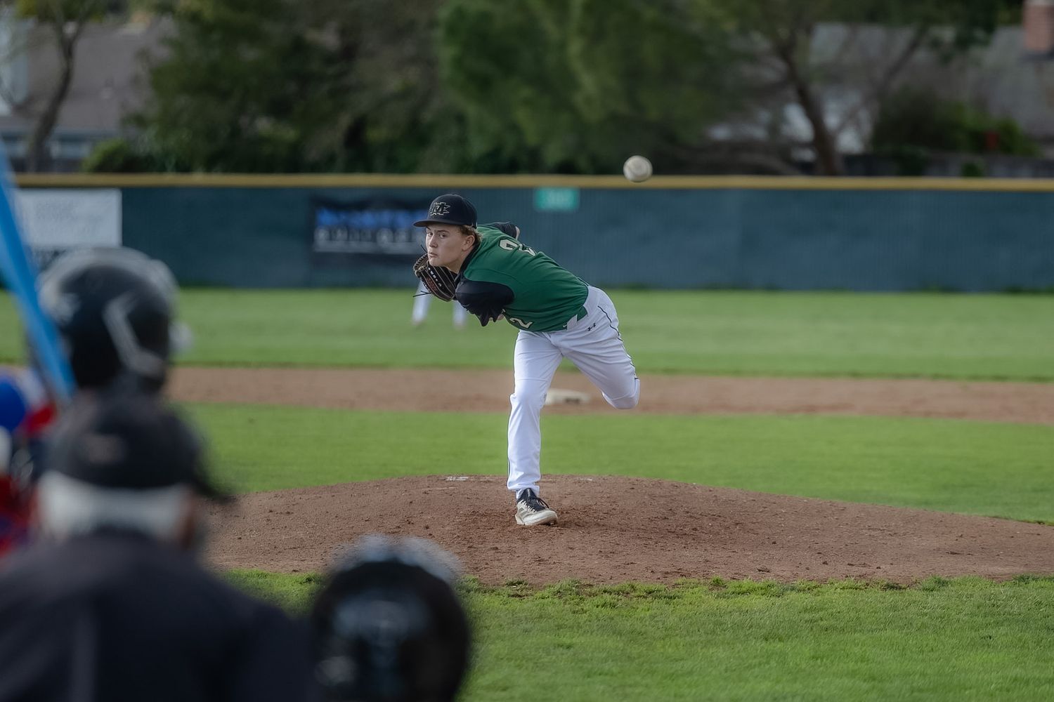 Baseball pitcher in green uniform mid-throw on mound during a game.