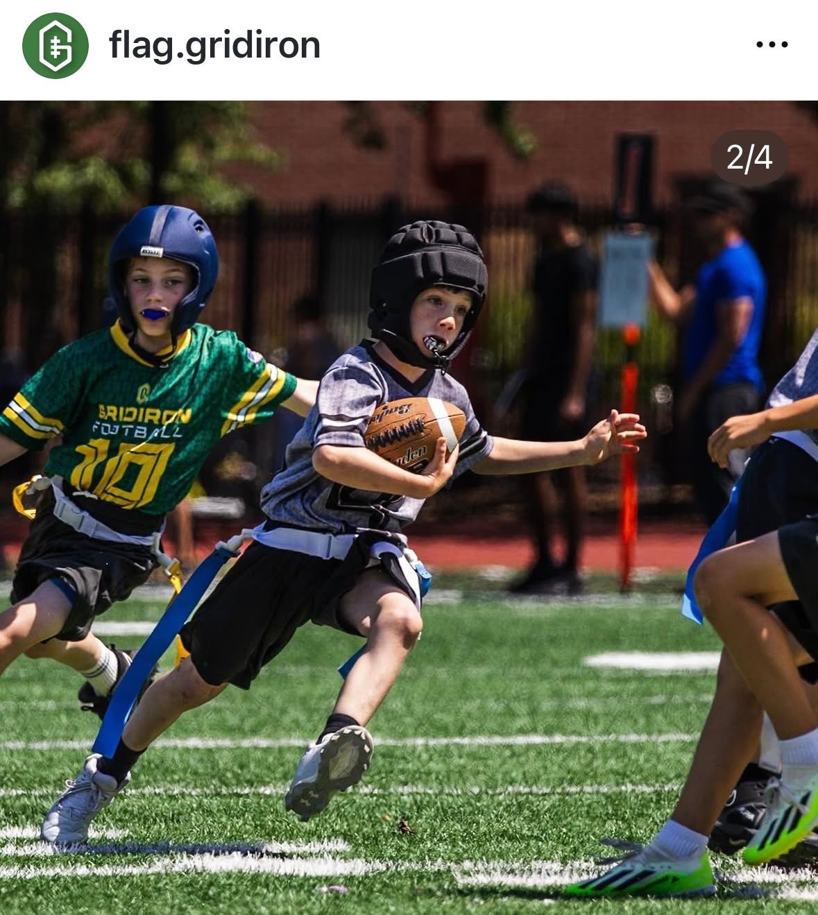 Kids playing flag football on a green turf field, with one player carrying the ball while others chase.
