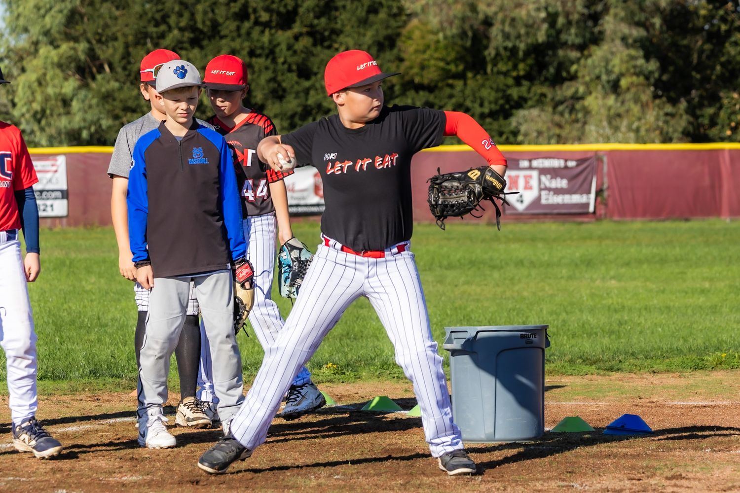 Baseball coach demonstrating pitching technique to young players during outdoor practice on a sunny day.