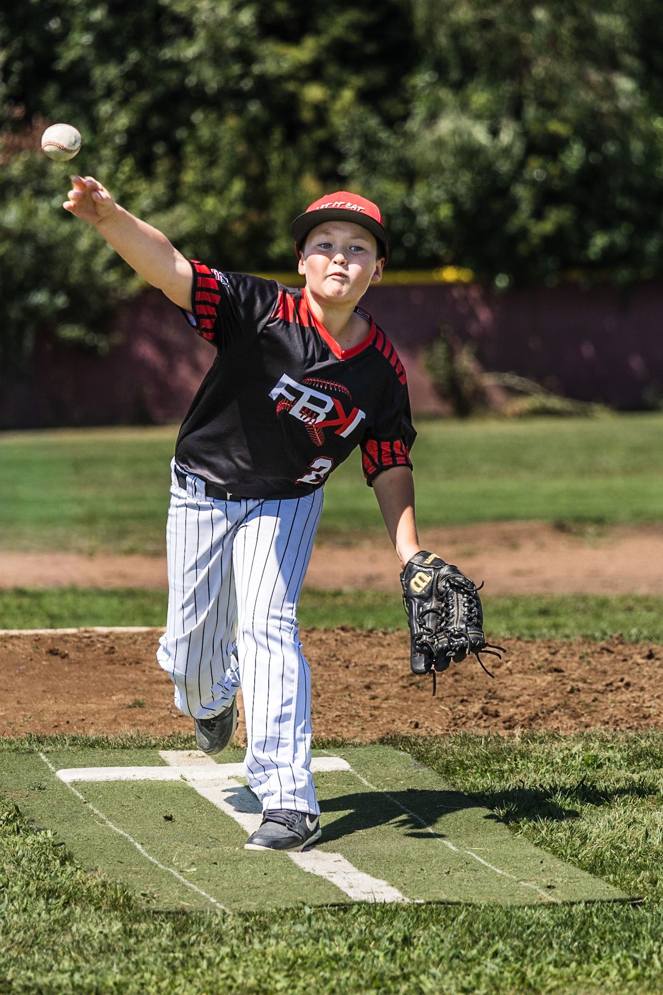 Young baseball pitcher in black FBJ uniform mid-throw on pitching mound during youth league game.