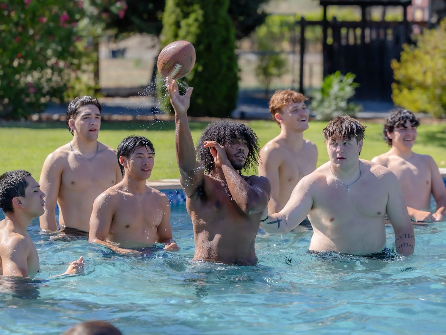 Group of young men playing football in a swimming pool on a sunny day.