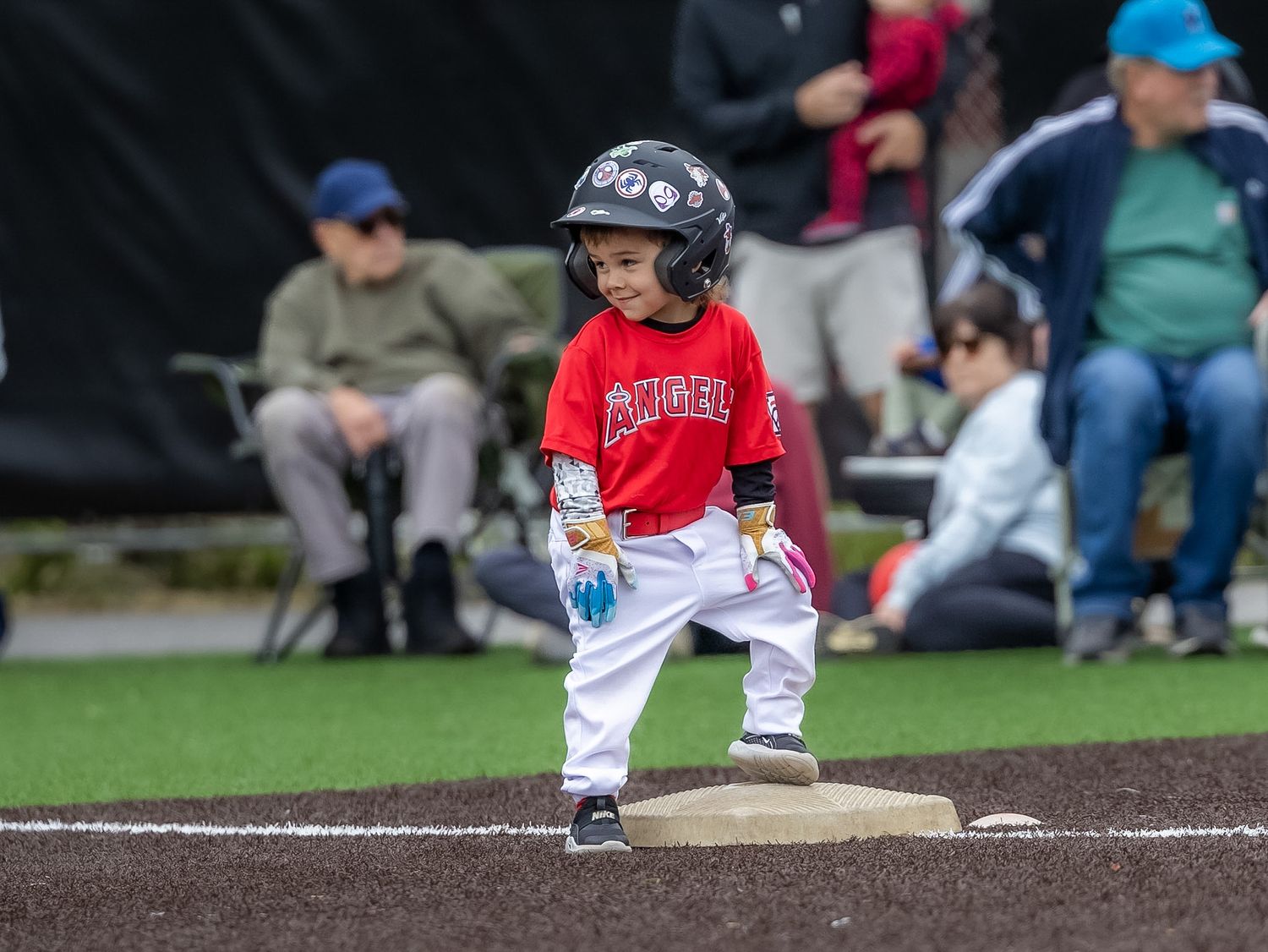 Young child in red baseball uniform and helmet stands on base during a youth baseball game.