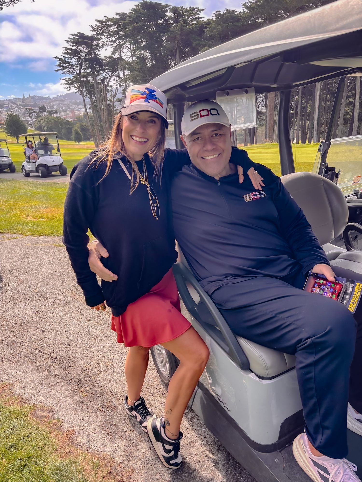 Two people smiling together near a golf cart on a lush green golf course on a cloudy day.