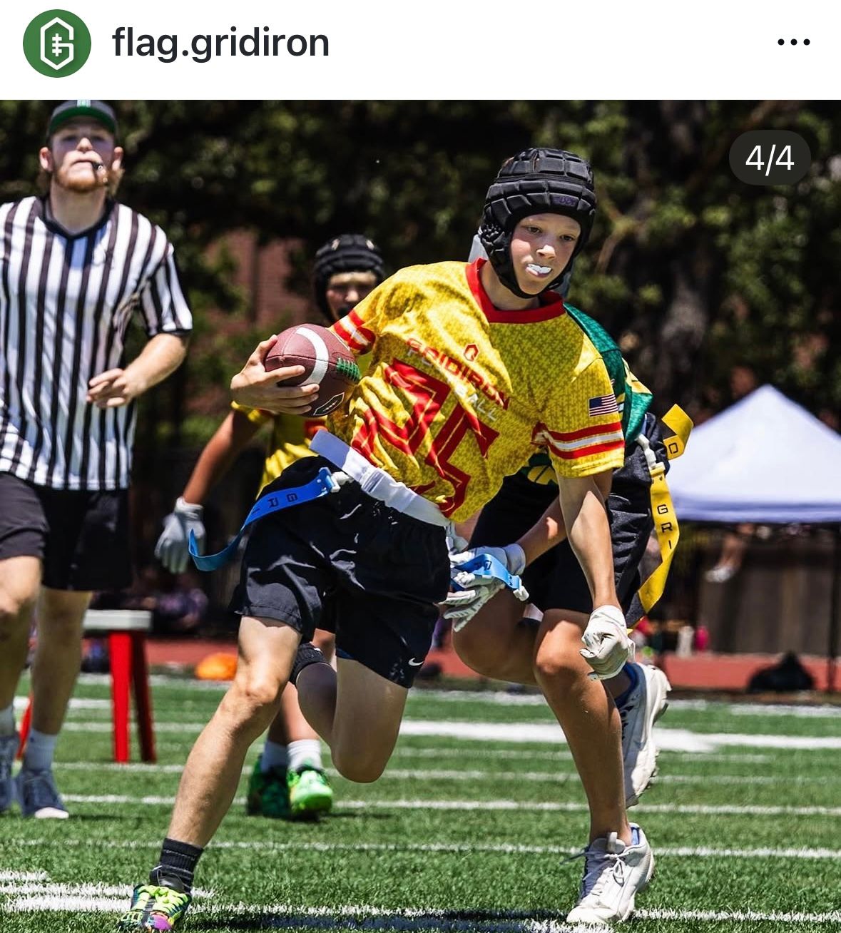 Young flag football player in yellow jersey runs with ball during sunny outdoor game, wearing helmet and flag belt.
