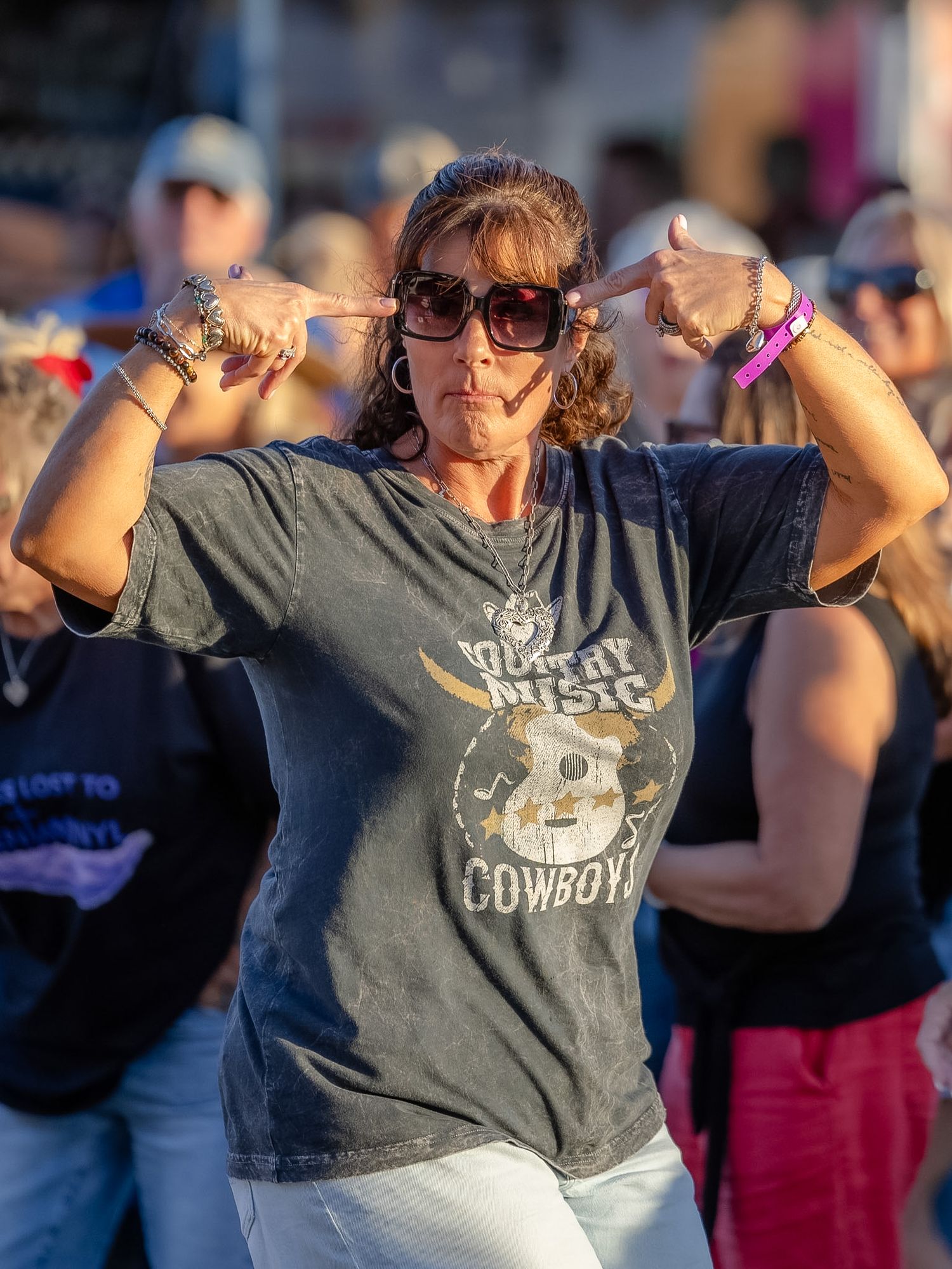 Woman in country music cowboy t-shirt posing with finger guns at an outdoor music festival.