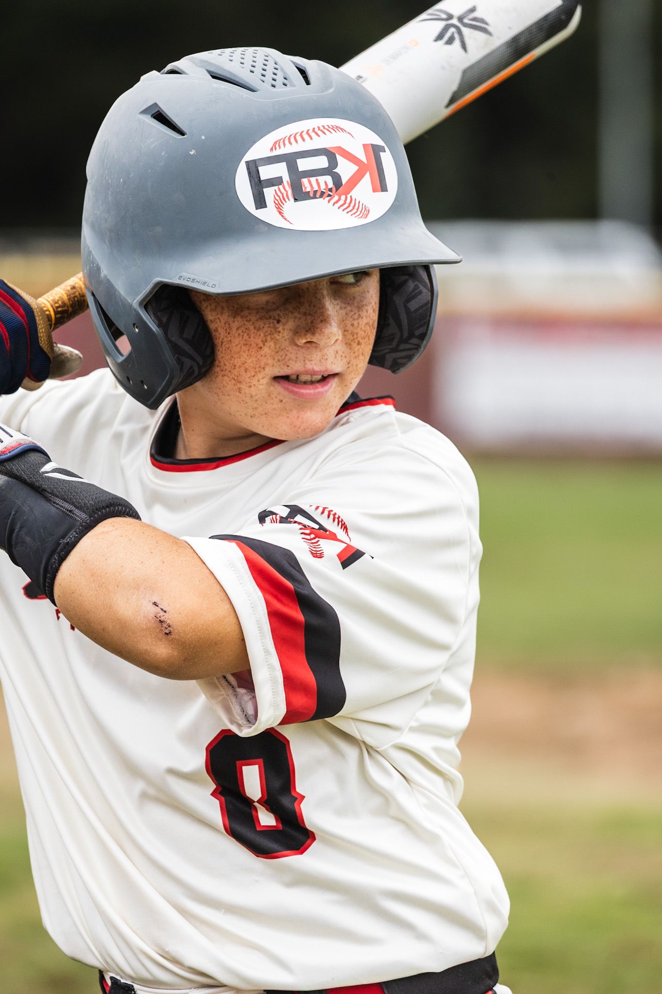 Young baseball player wearing FBK helmet and number 8 jersey stands ready at bat during a youth baseball game.