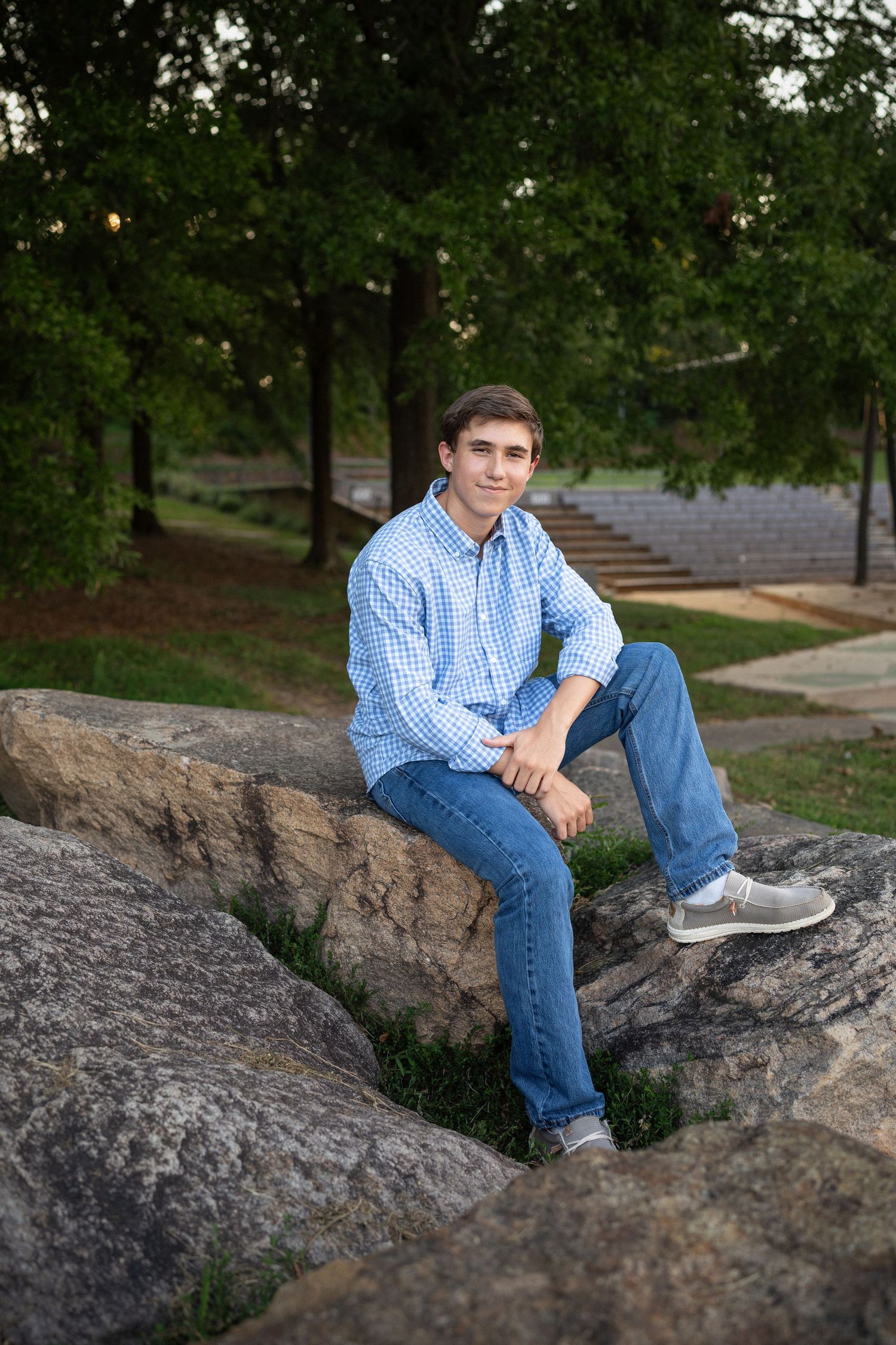 Sitting on large rocks in a blue checkered shirt and jeans during NCMA senior session
