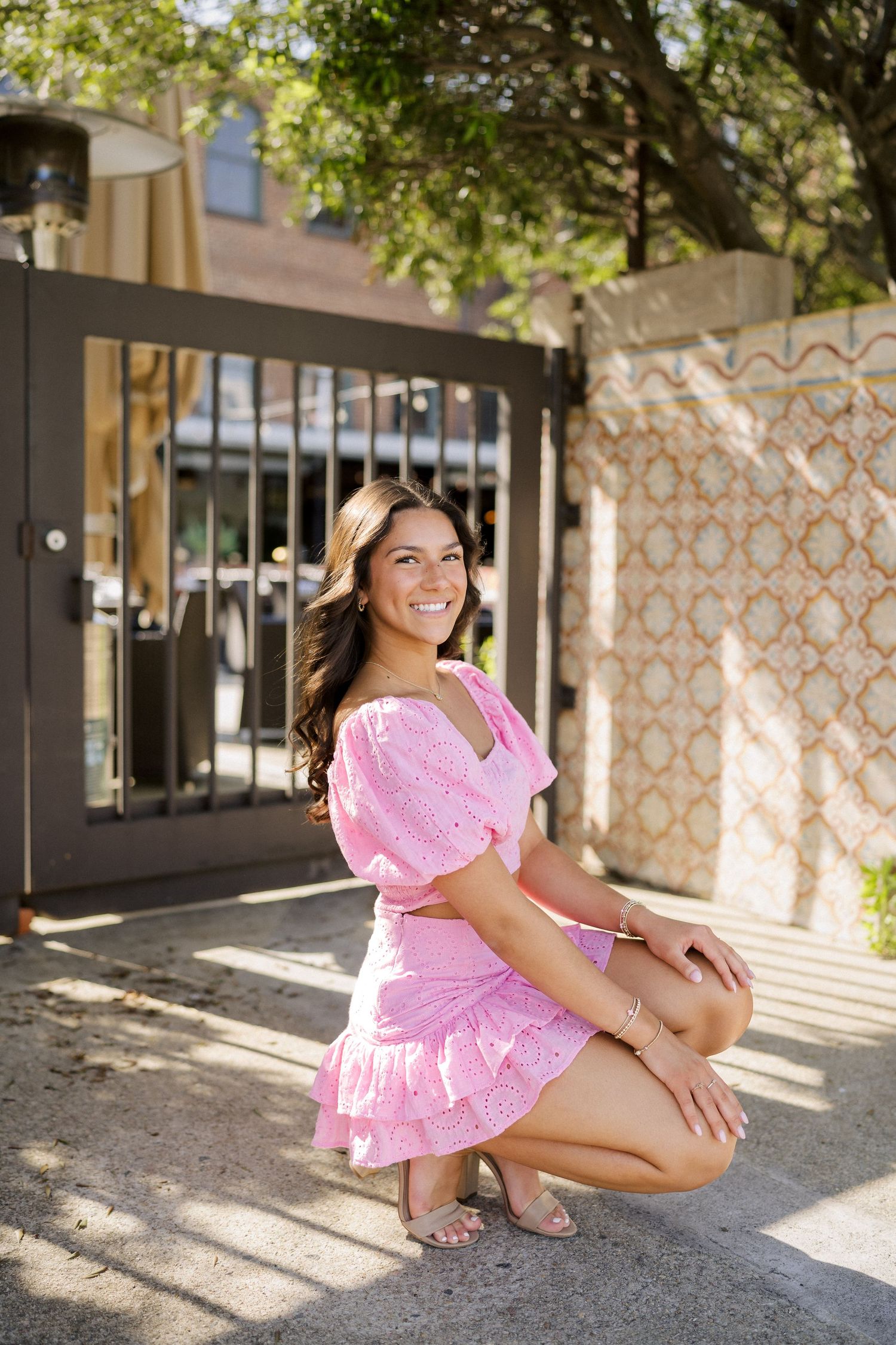High school senior girl in a pink outfit squatting for a portrait in downtown Raleigh.