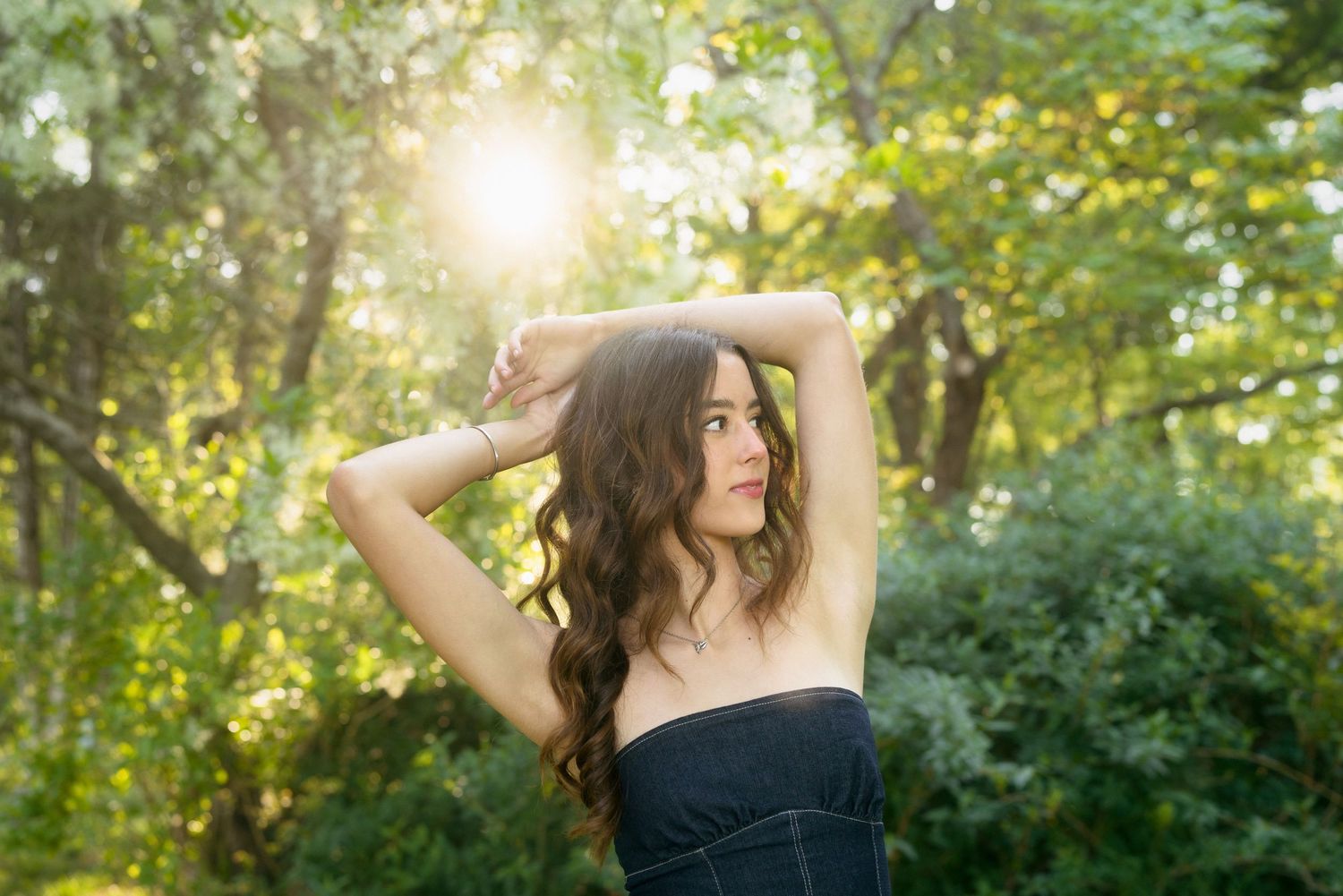 High school senior girl in a denim dress posing with her arms raised at Horseshoe Farm Preserve in Wake Forest.