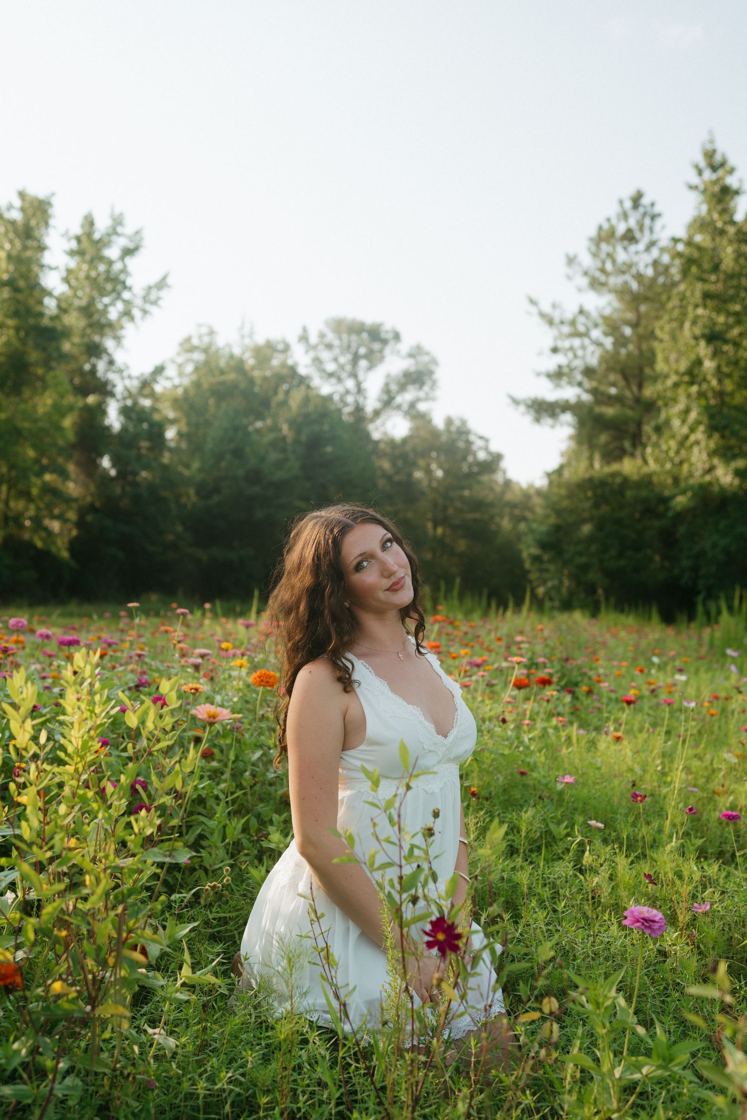 High school senior girl in a white dress sitting in the wildflowers in Raleigh, North Carolina.