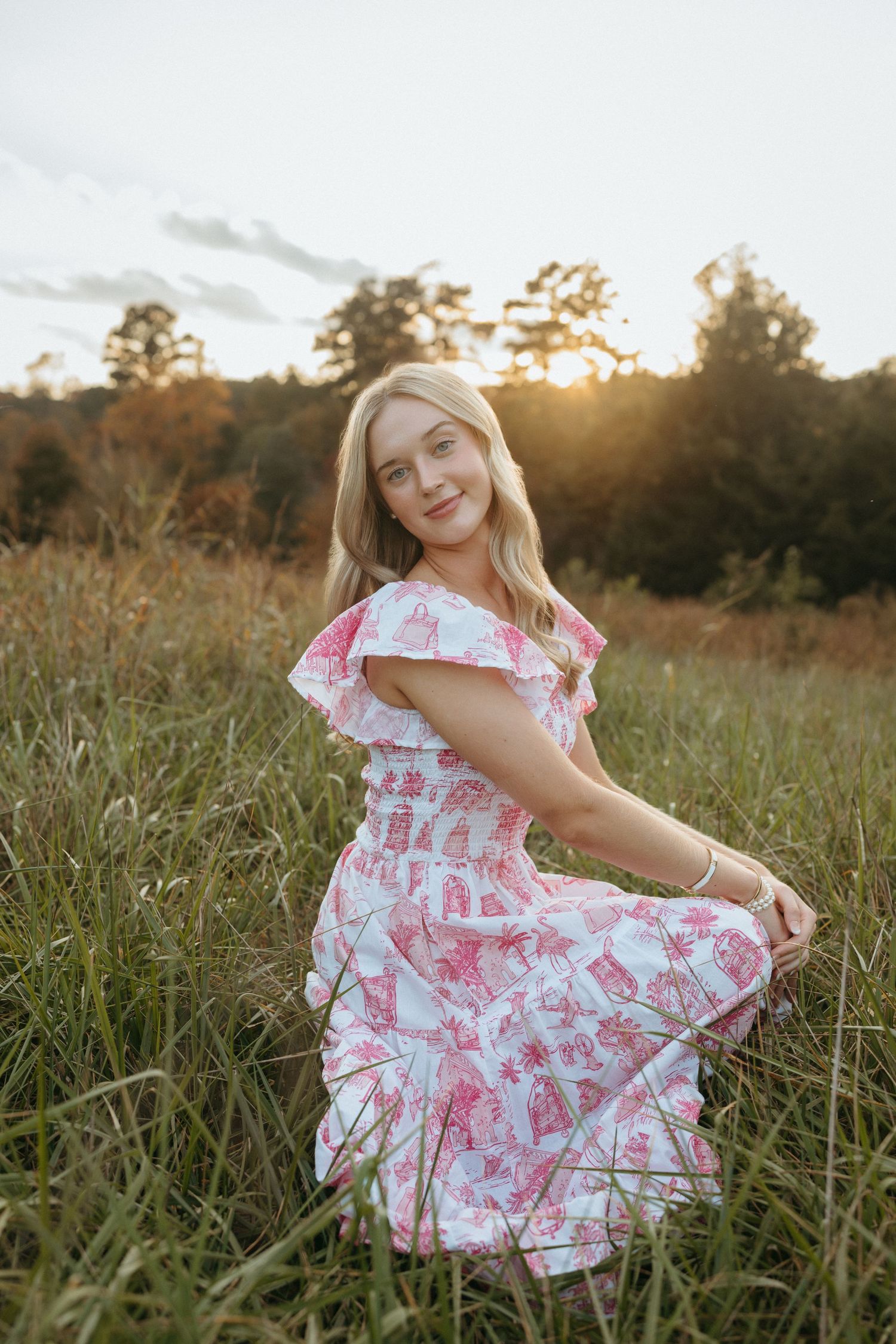 High school senior girl kneeling in the grass with sunlight behind her at Yates Mill in Raleigh.