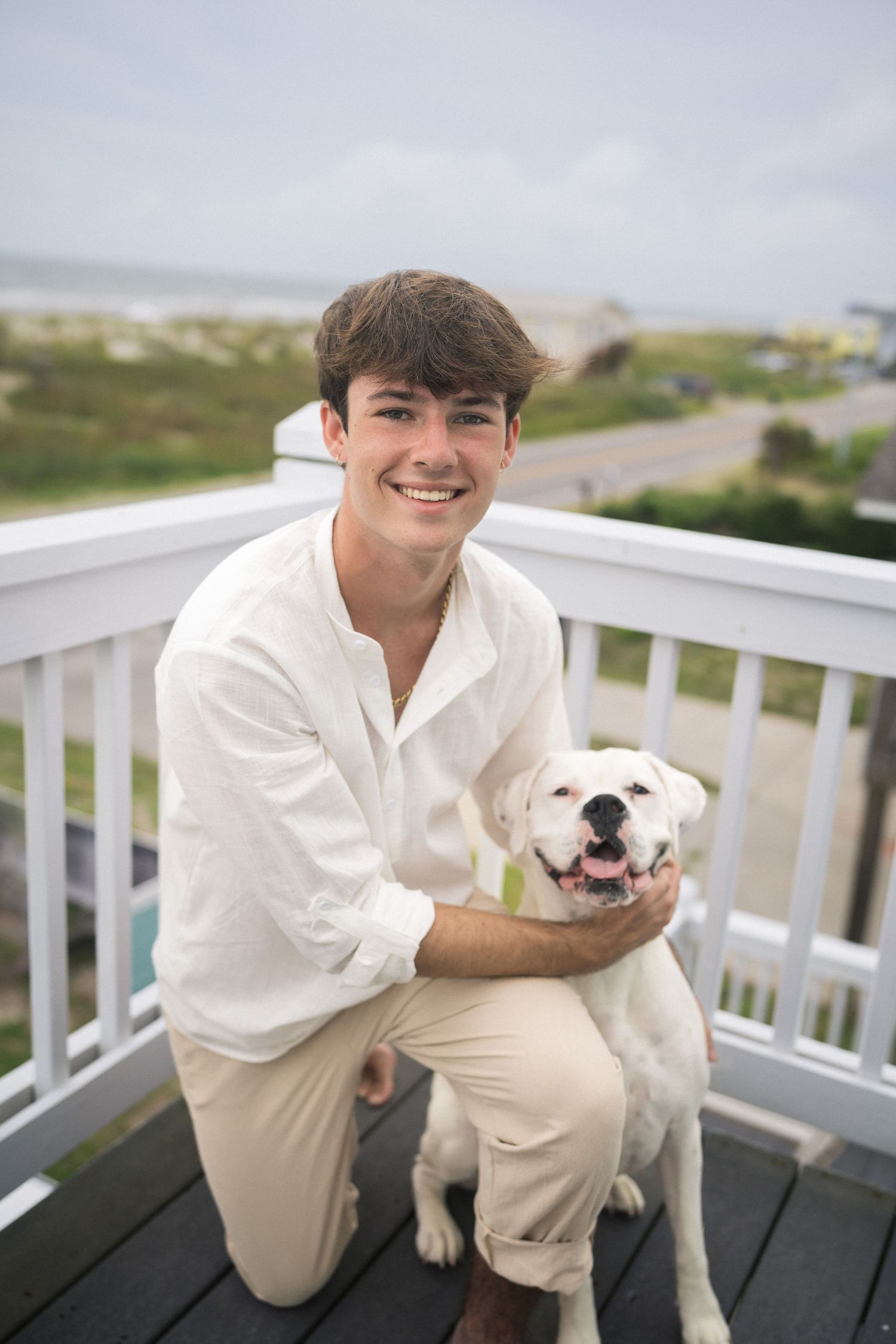 High school senior guy sitting with his dog on Oak Island Beach in North Carolina